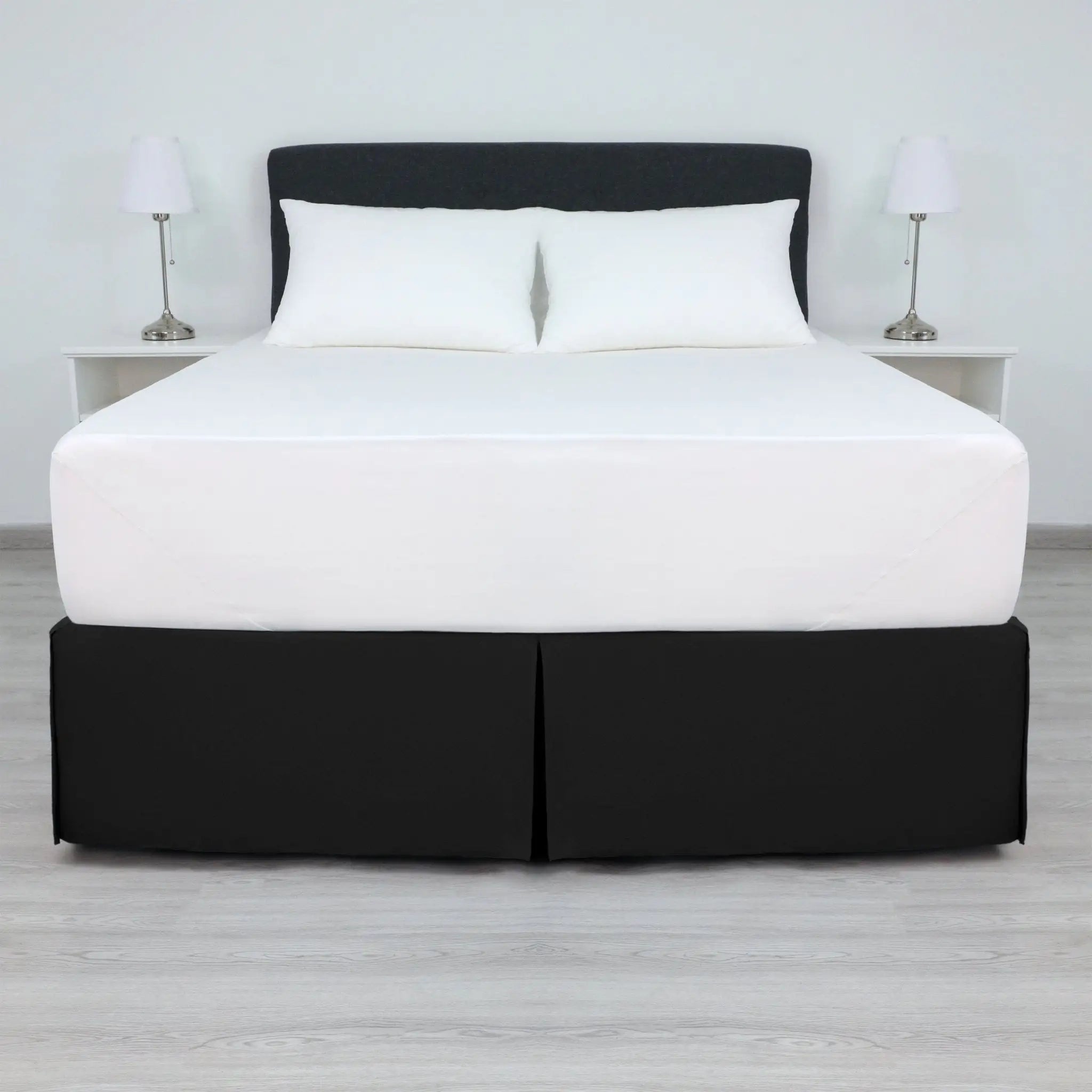 A bed with a white mattress and two white pillows, dressed in a black bed skirt.