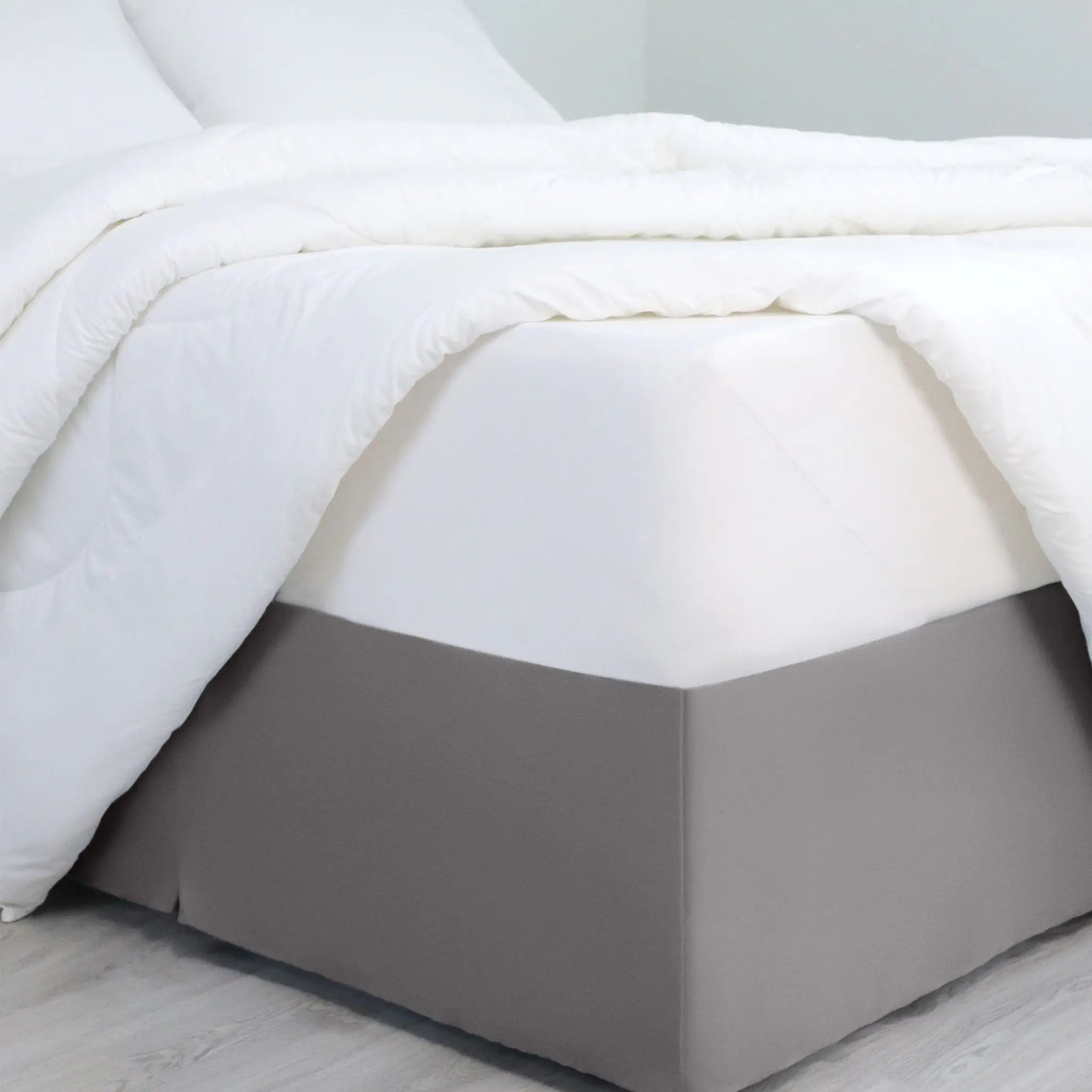 A bed dressed in white bedding, with a gray bed skirt covering the base of the frame.