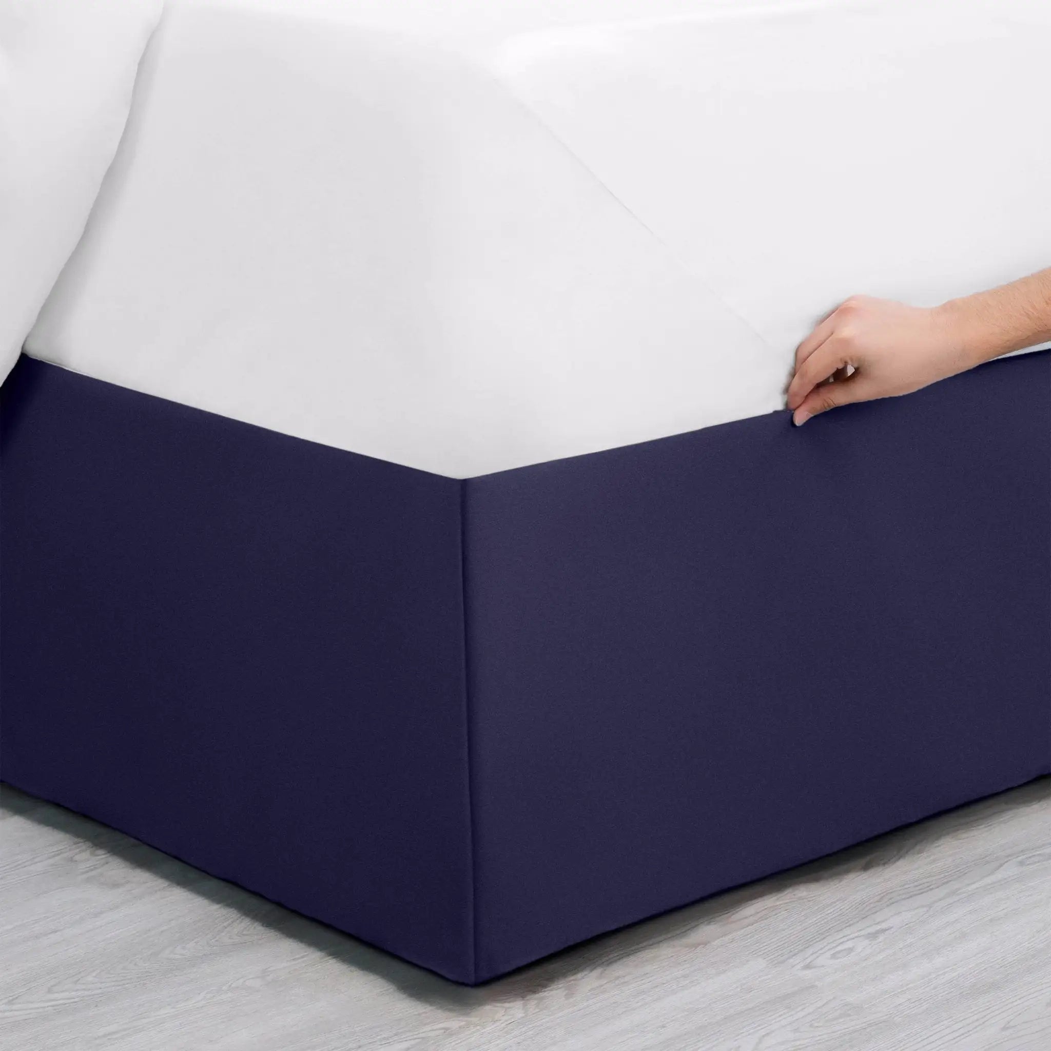 Navy bed skirt being adjusted on a bed with a white mattress.