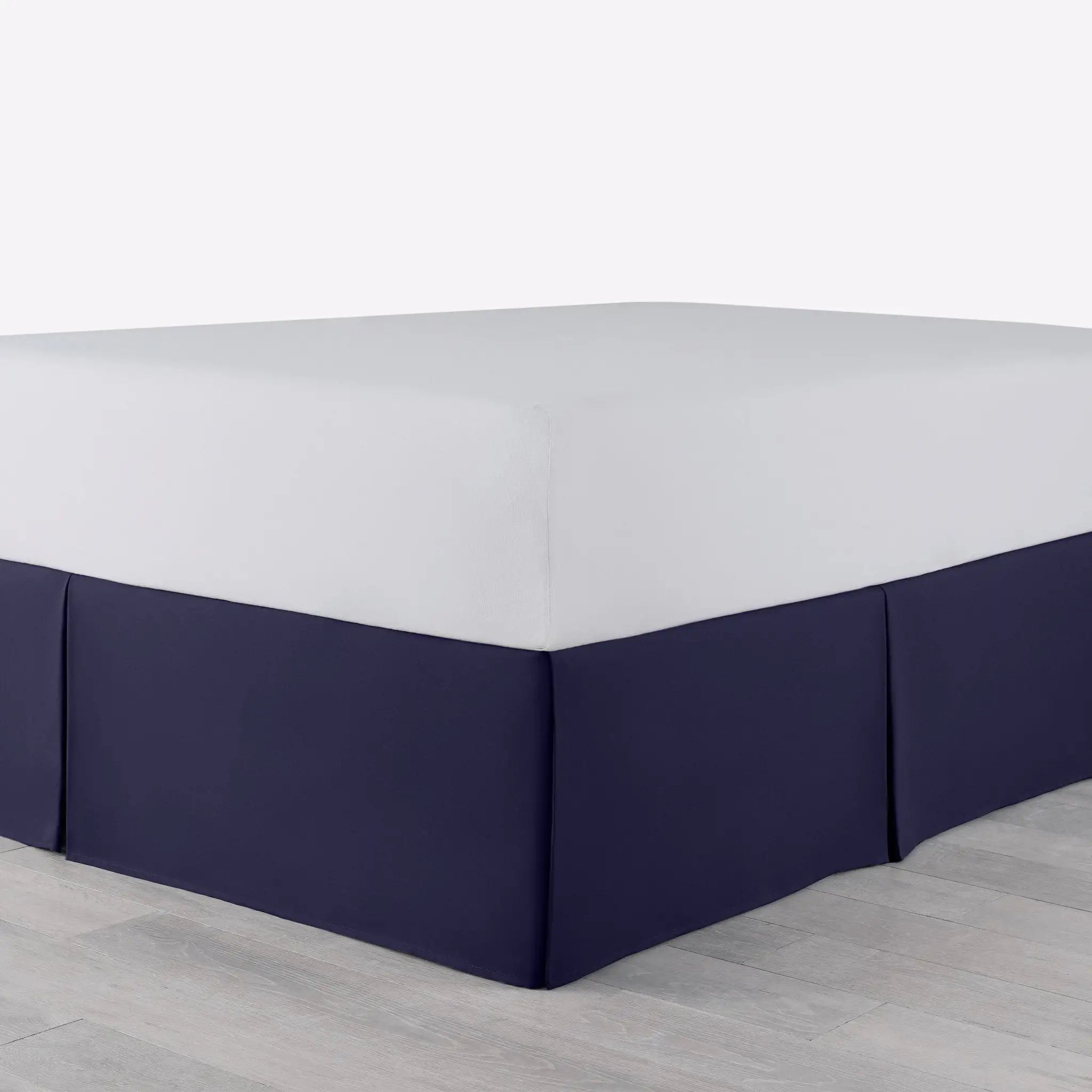 A bed with a fitted white sheet and a navy bed skirt, shown in a setting with light gray flooring.