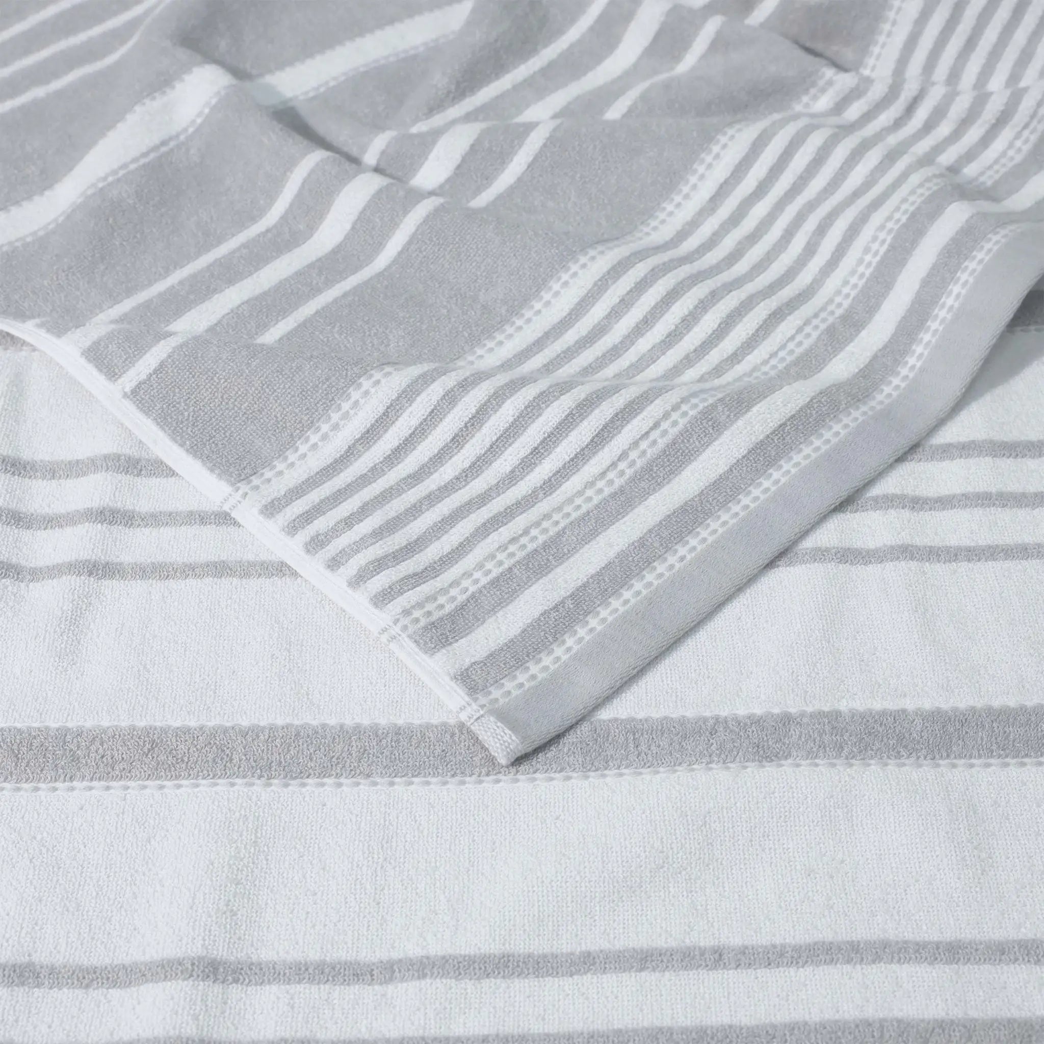 A close-up of a striped, grey towel textile and a folded corner showing the fabric texture.
