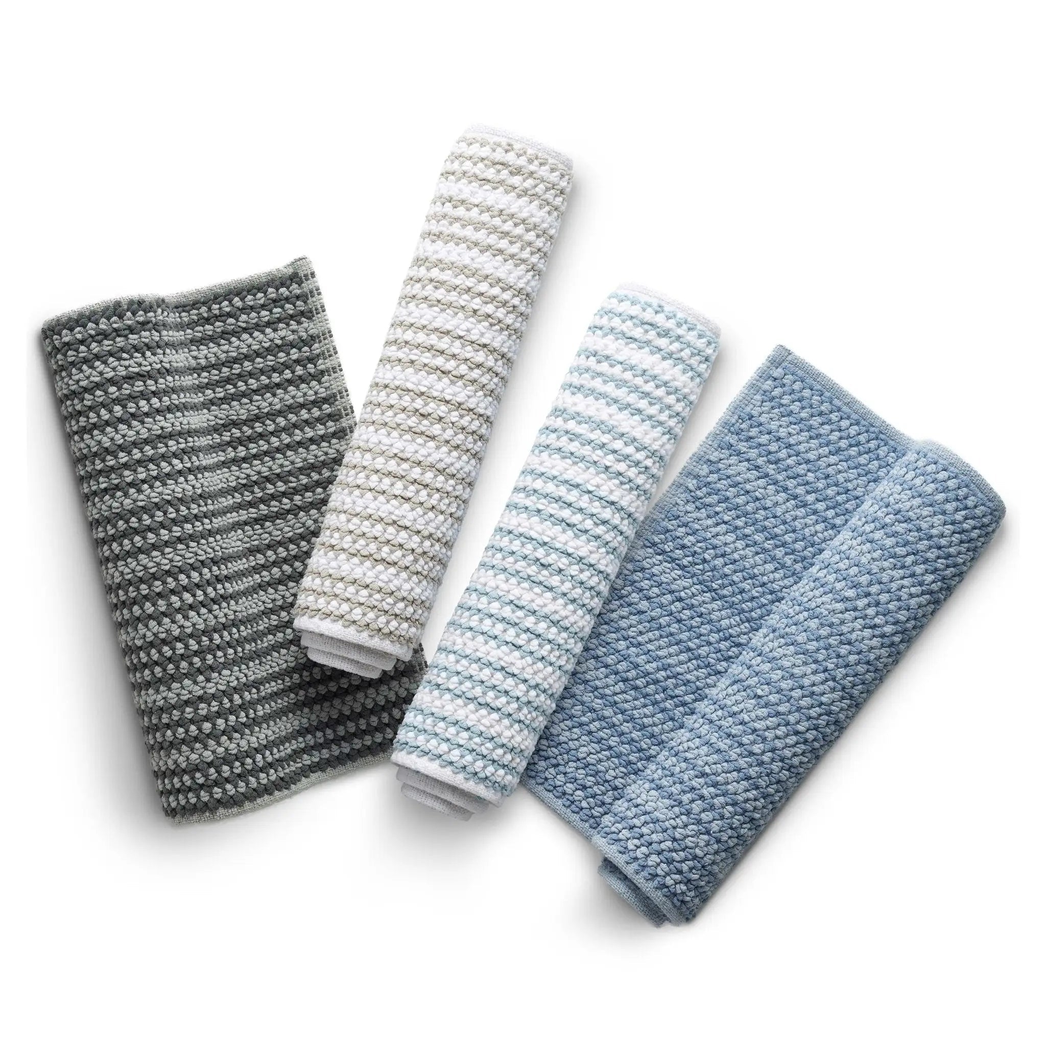 Four rolled bath rugs in sand, white, blue, and mineral, arranged diagonally on a white background.