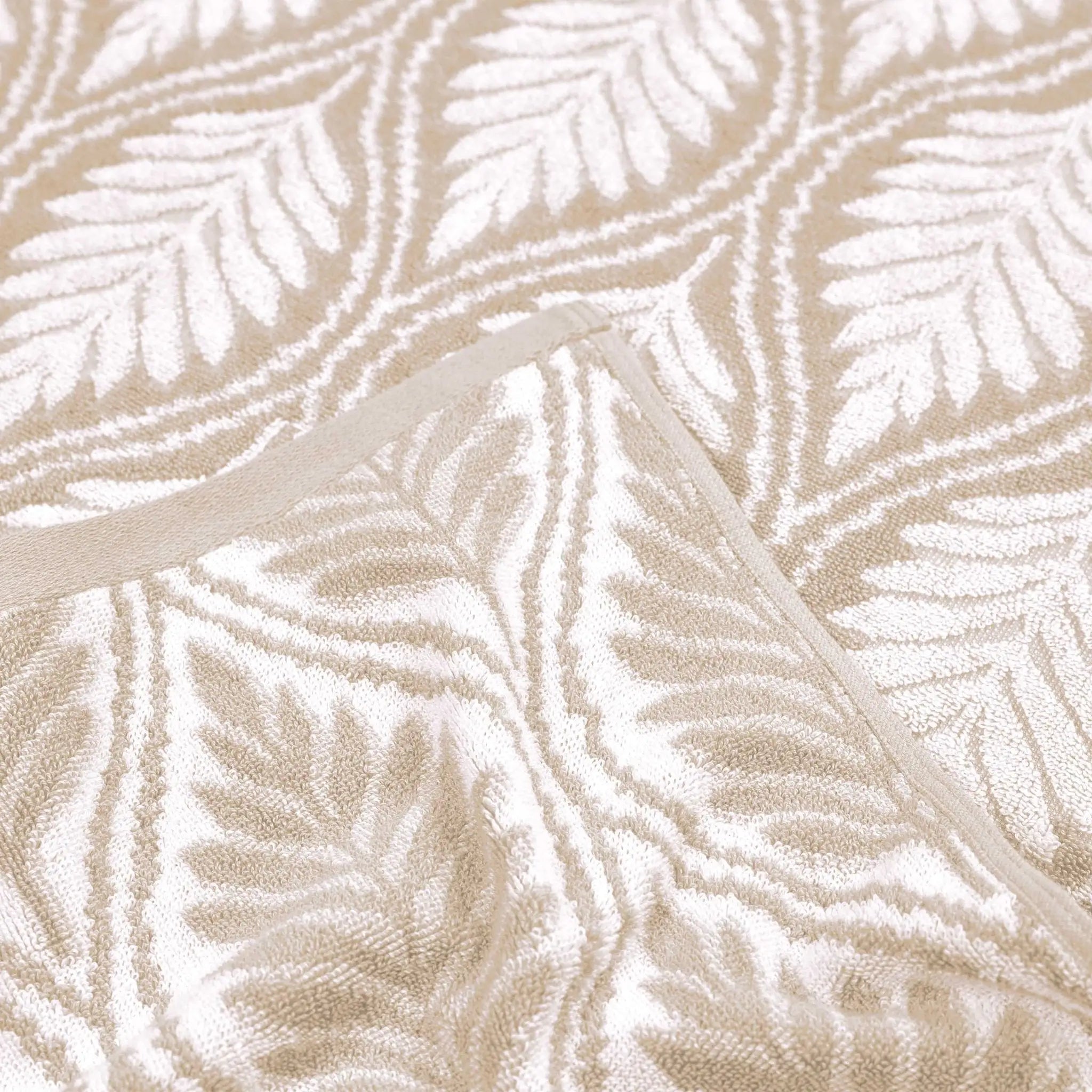 A close-up of a sand and white jacquard fabric with a repeating leaf pattern and a solid beige trim.
