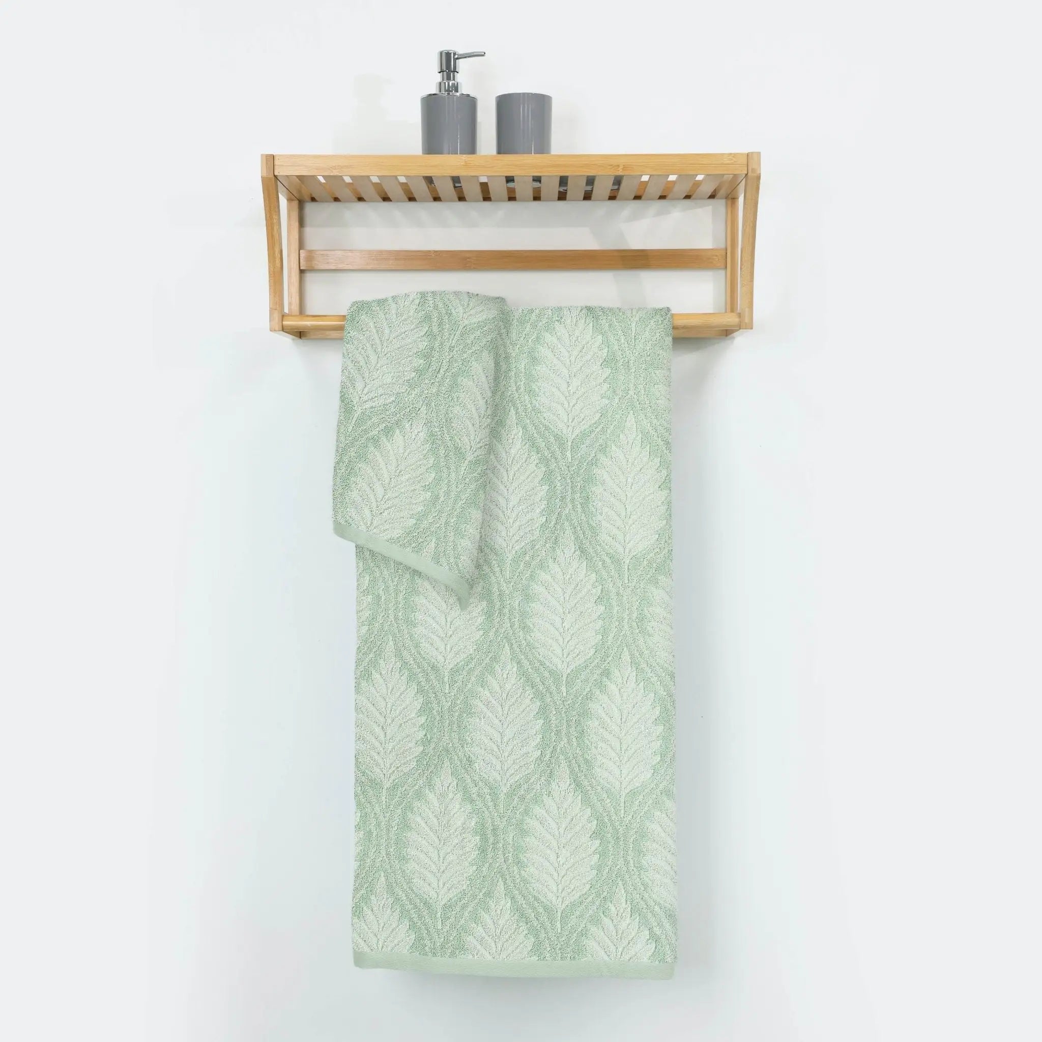 Green patterned bath towel hanging on a wooden towel rack against a white wall.
