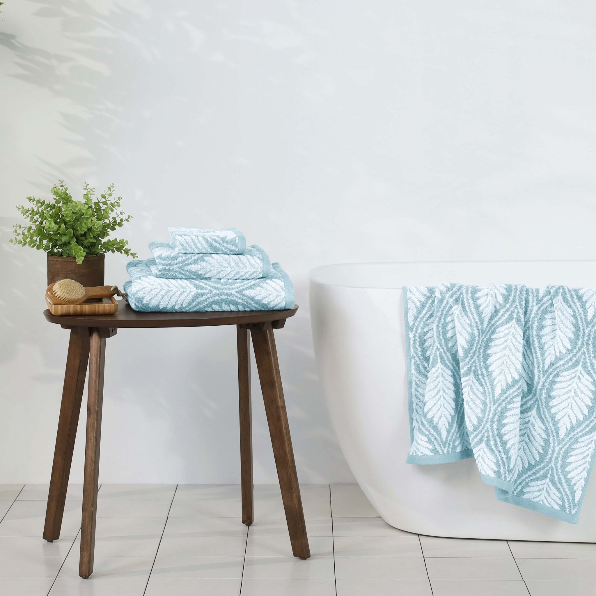 Mineral towels with leaf pattern on a wooden stool against a white wall.