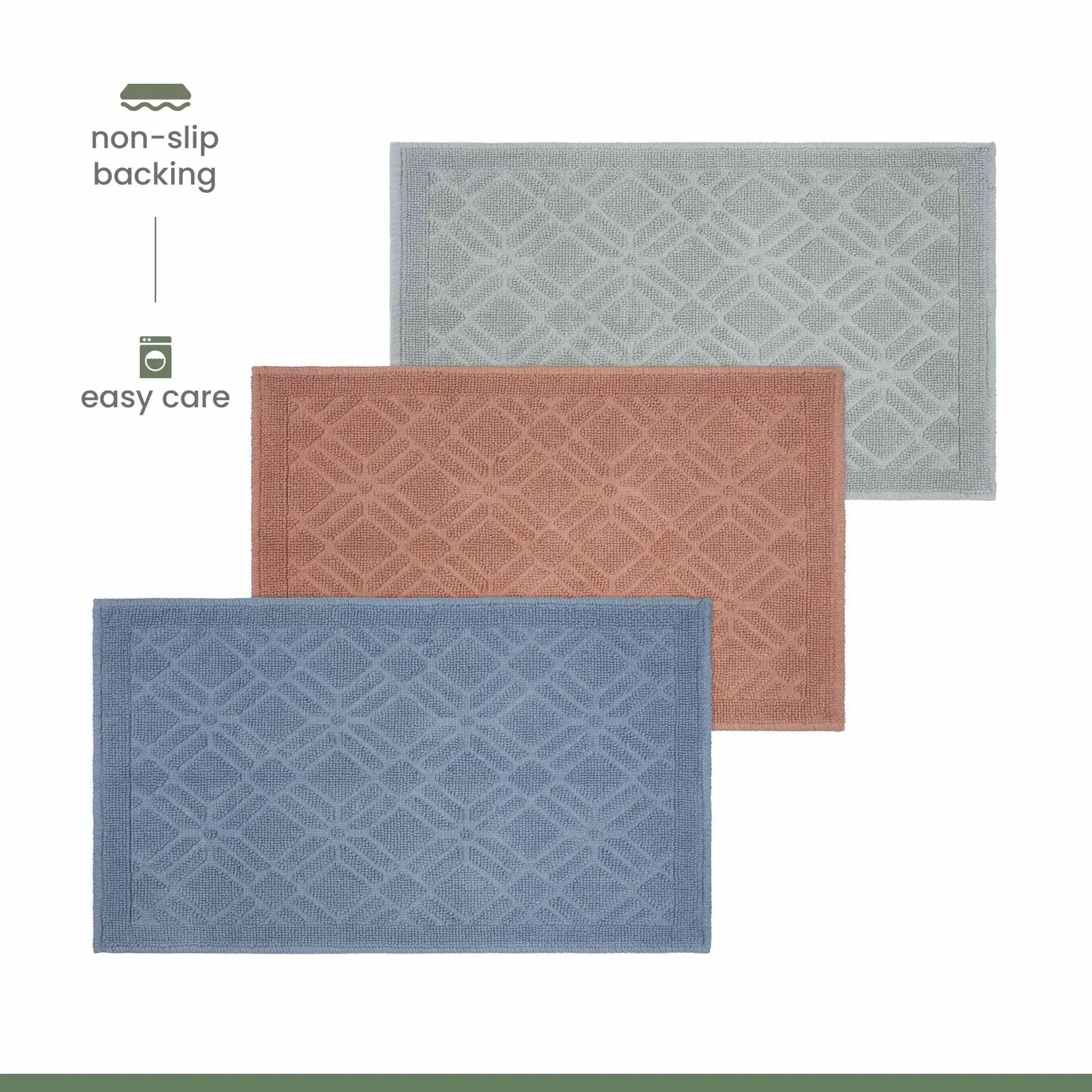 Three rectangular bath rugs with a raised geometric pattern are shown on a white background, labeled with features: non-slip backing and easy care. The mats are in blue, dusty rose, and light gray, arranged diagonally.