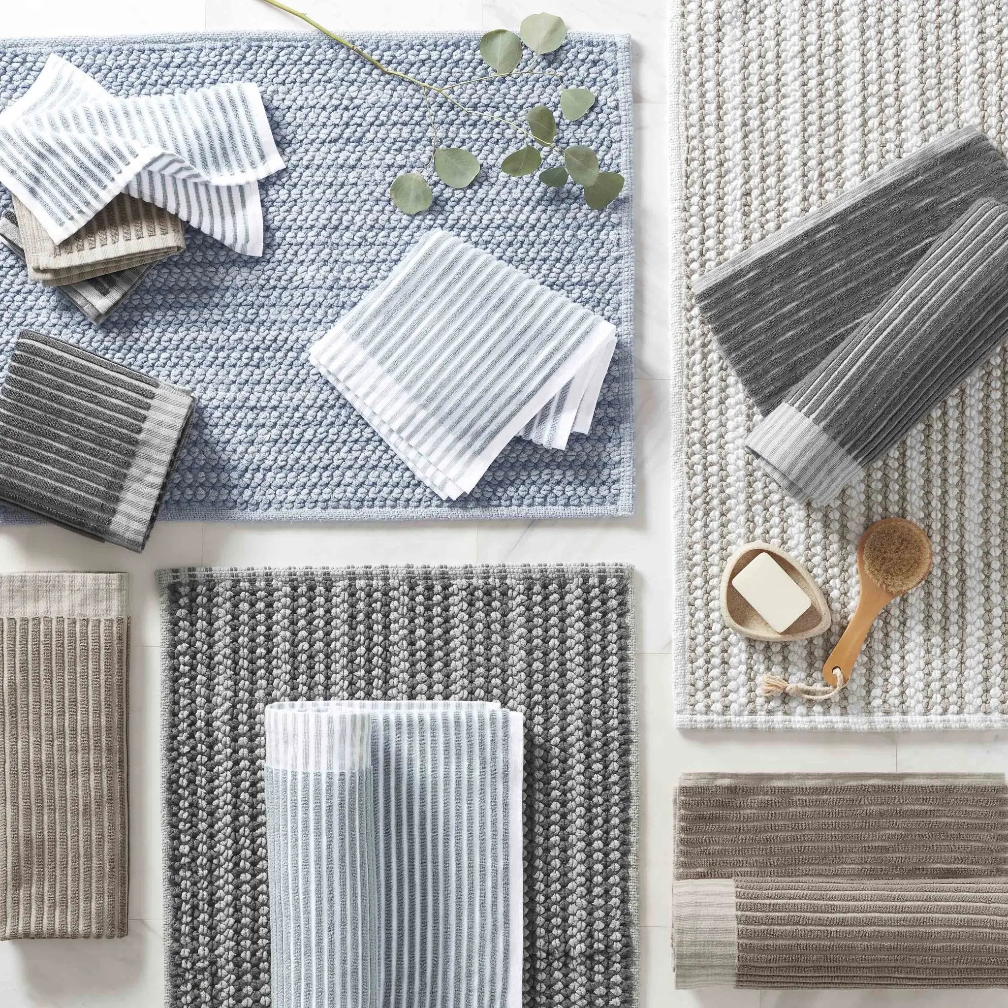 A styled flat-lay of multiple textured bath towels and bath mats in neutral tones.