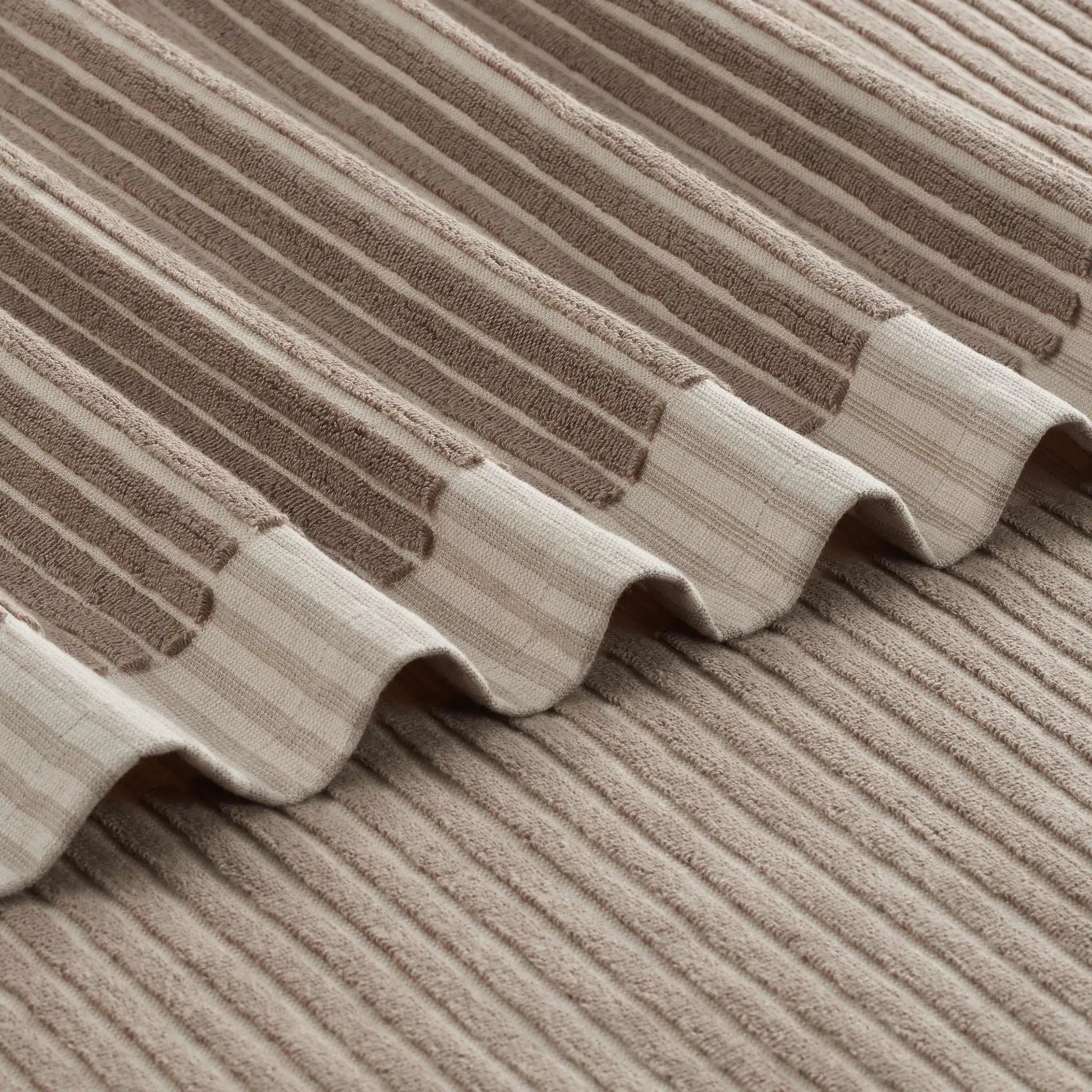 Close-up of a tan bath towel, showing the texture and wavy stitched edge.