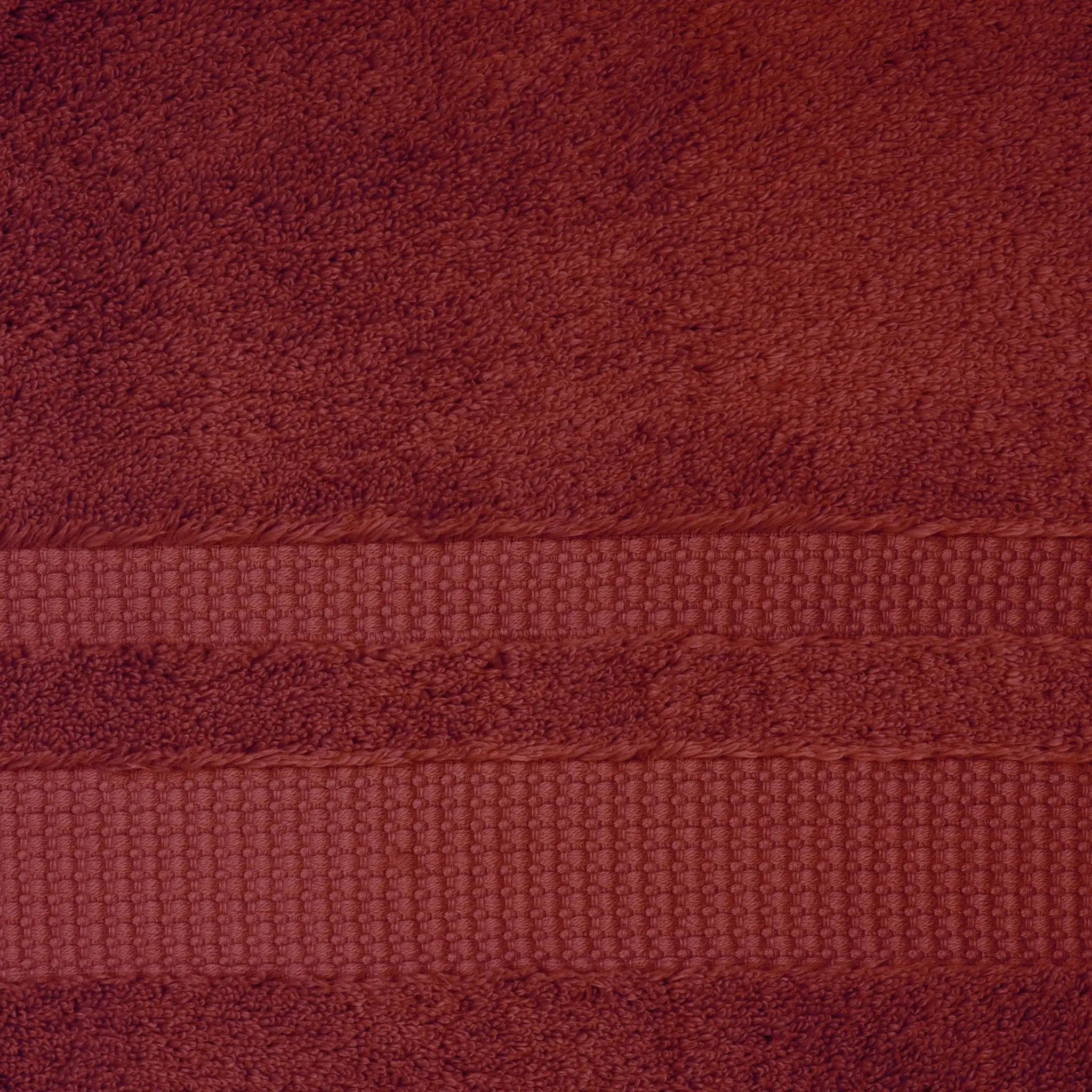 A close-up of a red bath towel showing its textured terry cloth body and a horizontal woven border stripe.