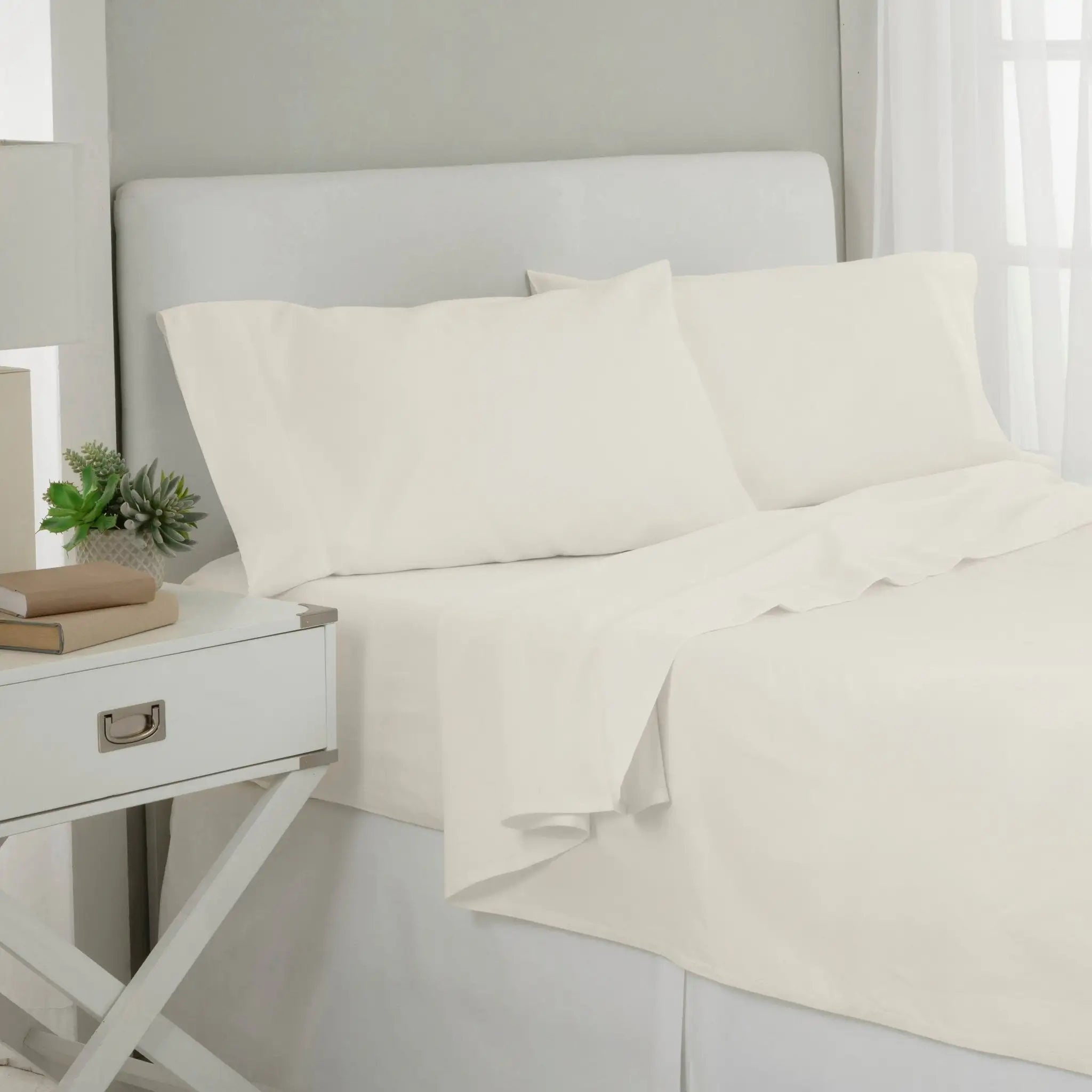 White cotton sheet and pillowcase set on a bed with a white upholstered headboard.