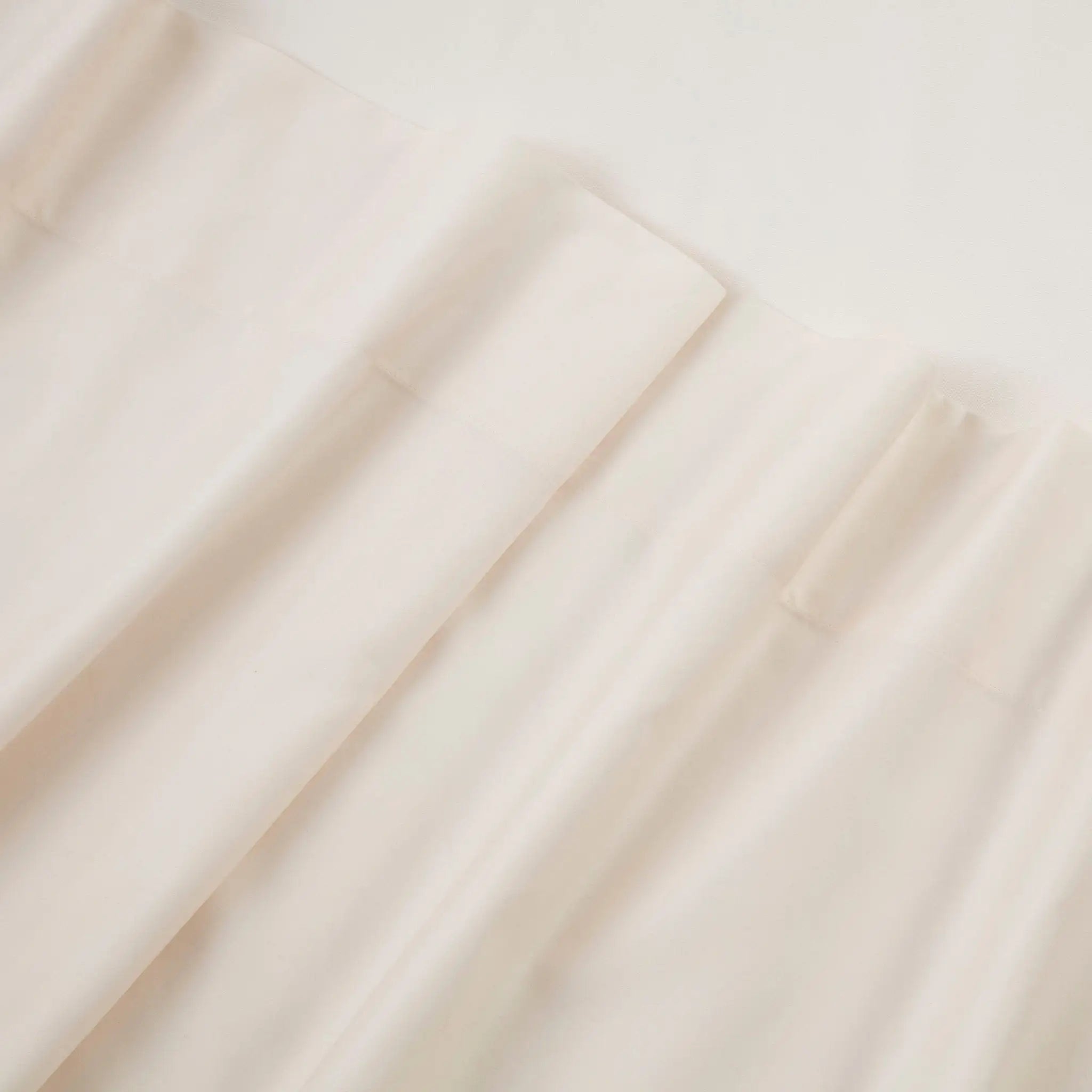 A close-up of draped off-white or cream-colored fabric with soft folds and a smooth texture.
