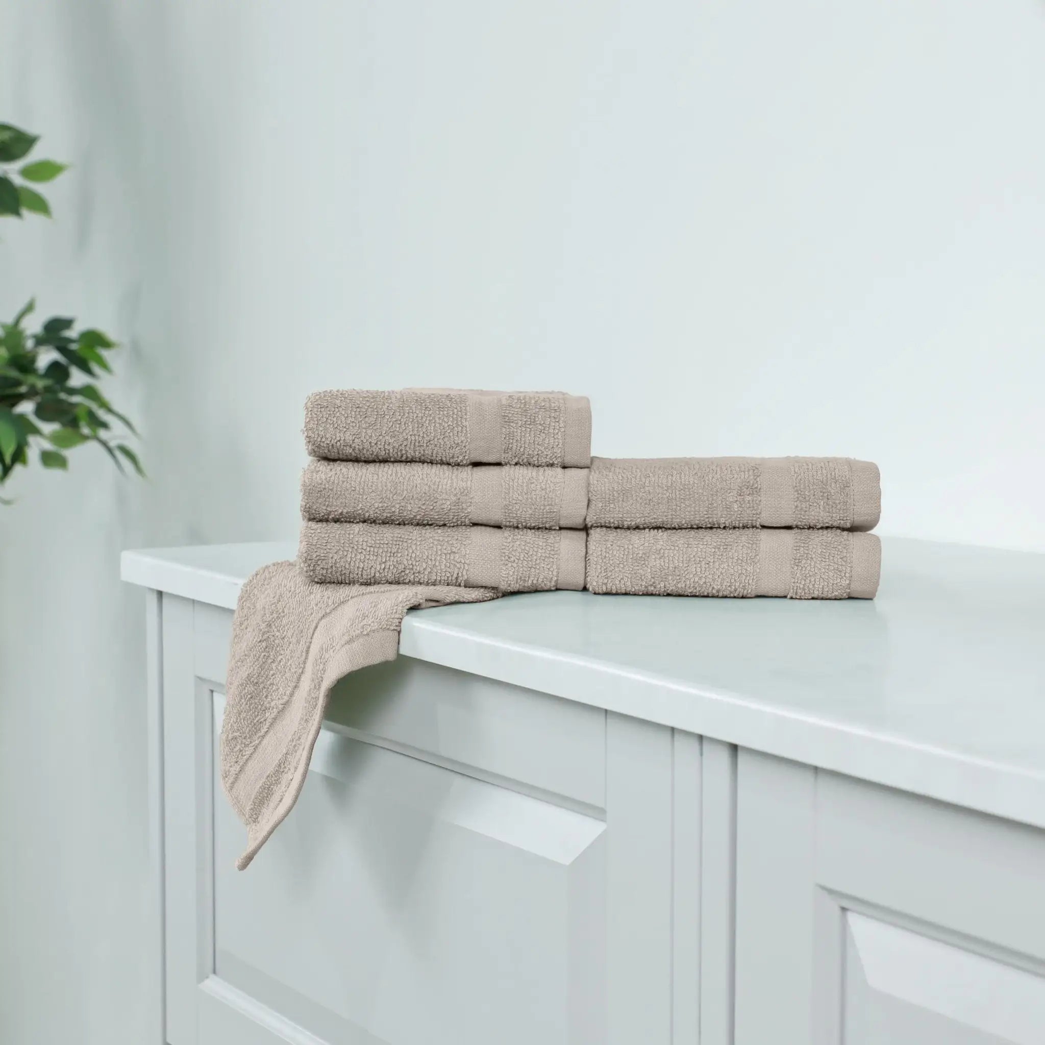 A stack of beige cotton washcloth, including a folded wash towel draped over the edge.