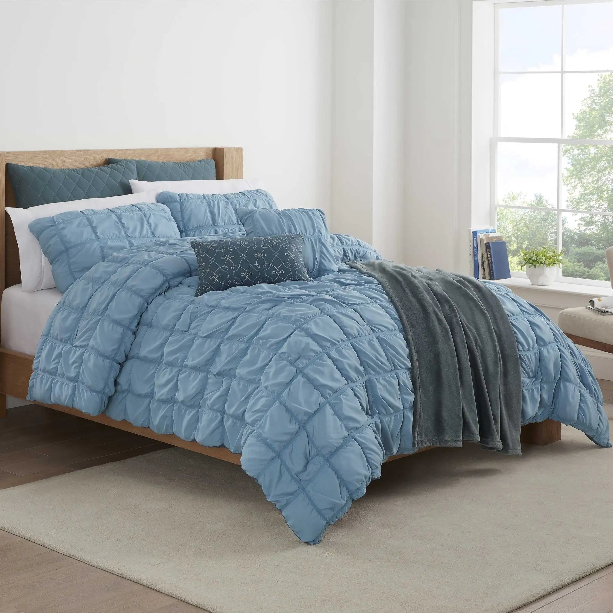 Blue textured comforter set on a bed in a bright bedroom with large windows.