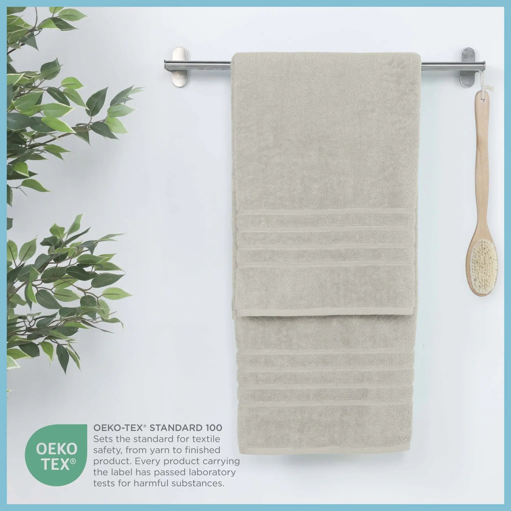 A sand-colored textured bath sheet hangs from a silver metal towel bar on a white wall. An OEKO-TEX certification badge is shown in the lower-left corner.