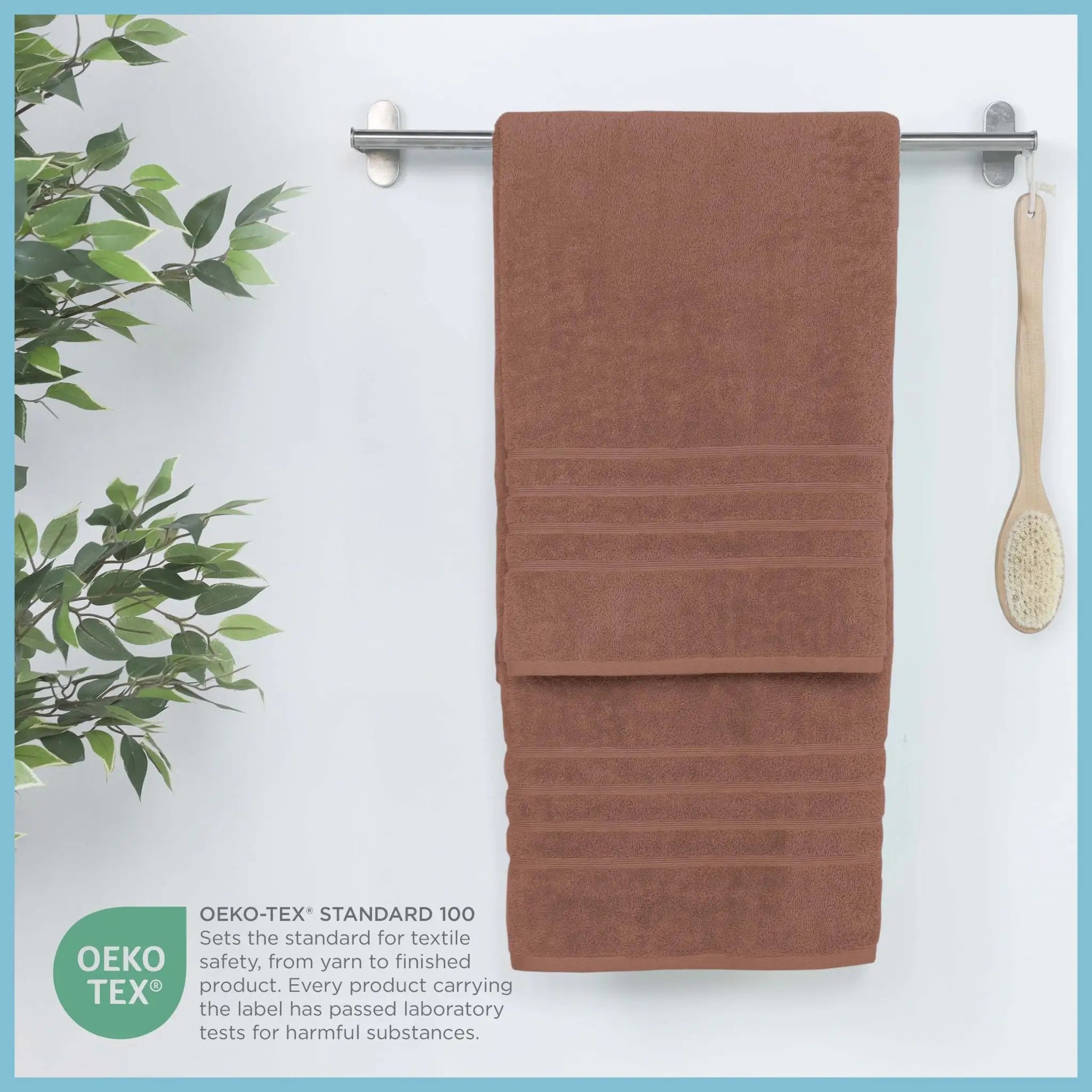 Terracotta bath sheet hanging on a rack with a plant and brush in the background, featuring OEKO-TEX certification.
