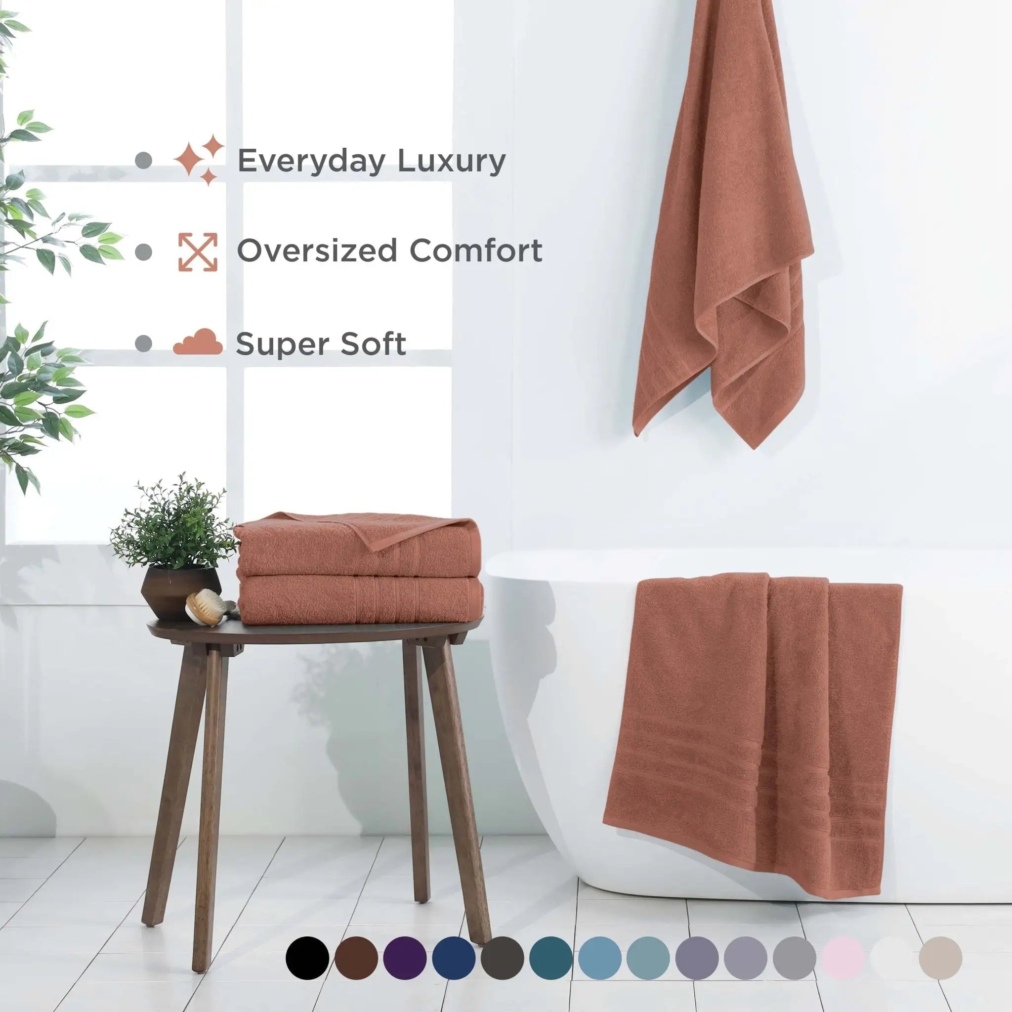 A set of terracotta-colored bath sheets, including a folded stack on a wooden table, with marketing text 'Everyday Luxury', 'Oversized Comfort', and 'Super Soft' on the left, and a color swatch circle row at the bottom.