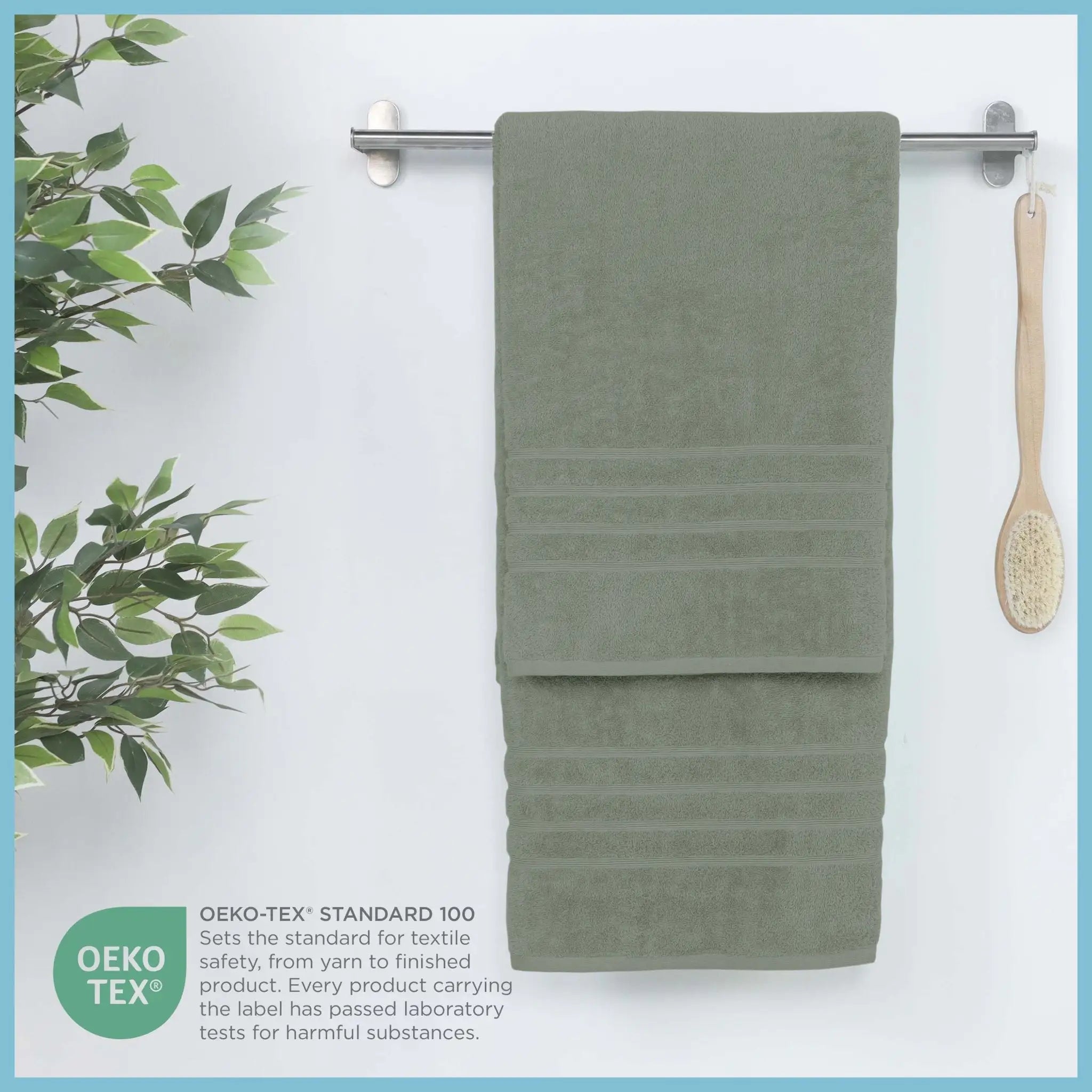 Sage bath sheet hanging on a rack with a plant and brush on a white background, featuring OEKO-TEX certification.