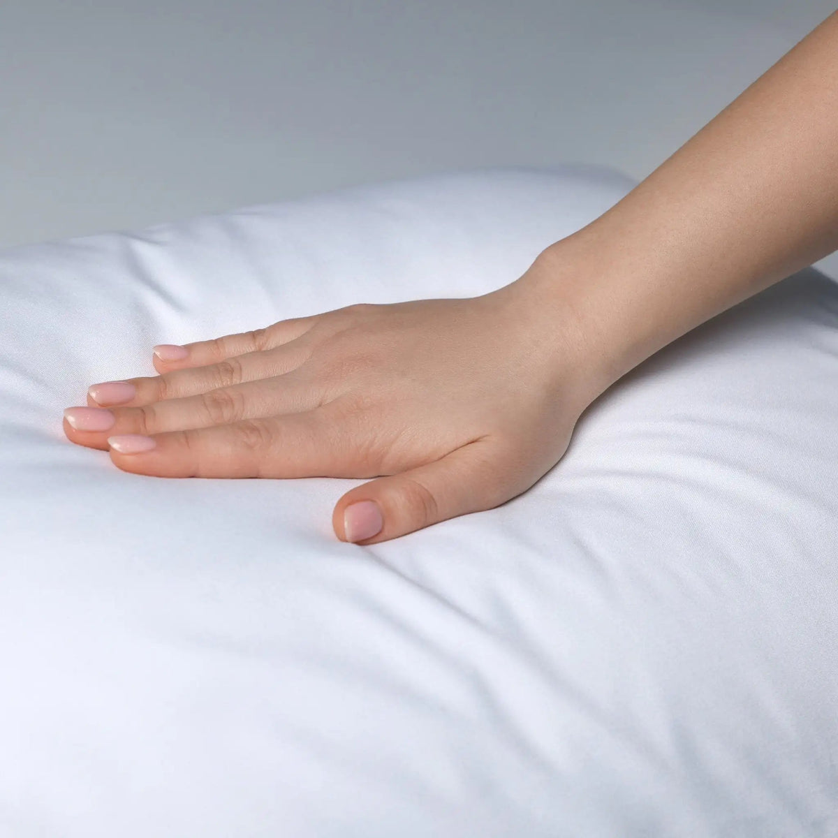 Hand resting on a white pillow with a neutral background