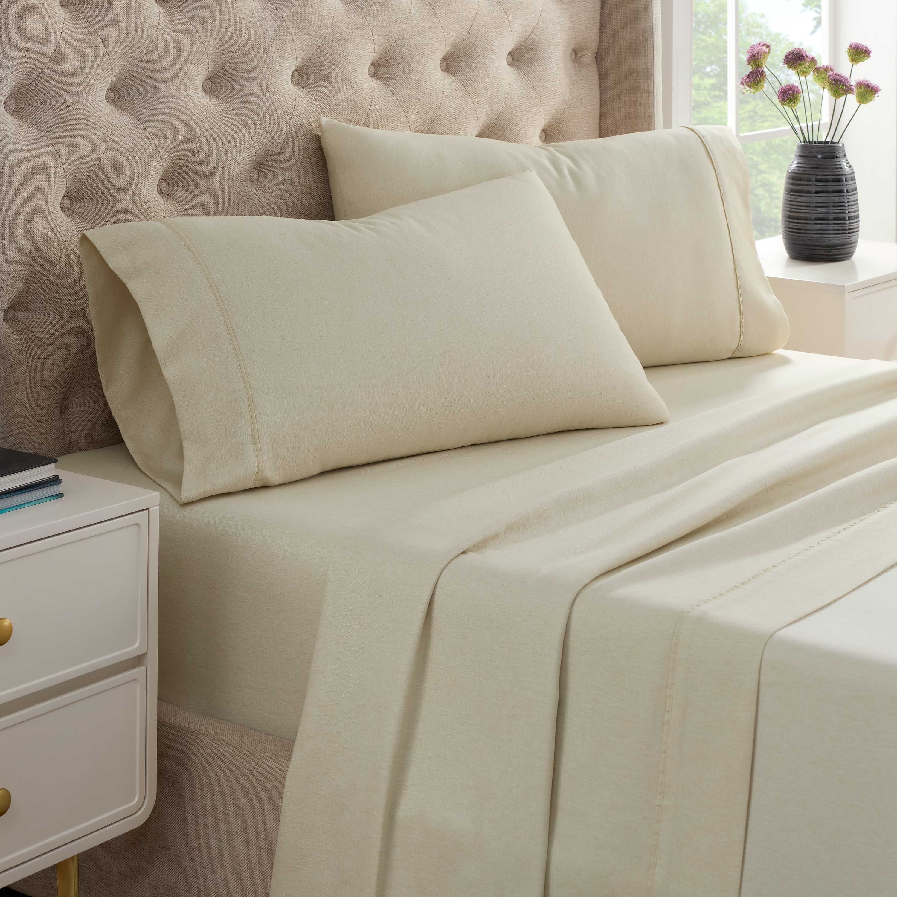 Light beige herringbone sheet set with two matching pillowcases on a bed next to a nightstand and a vase of flowers.