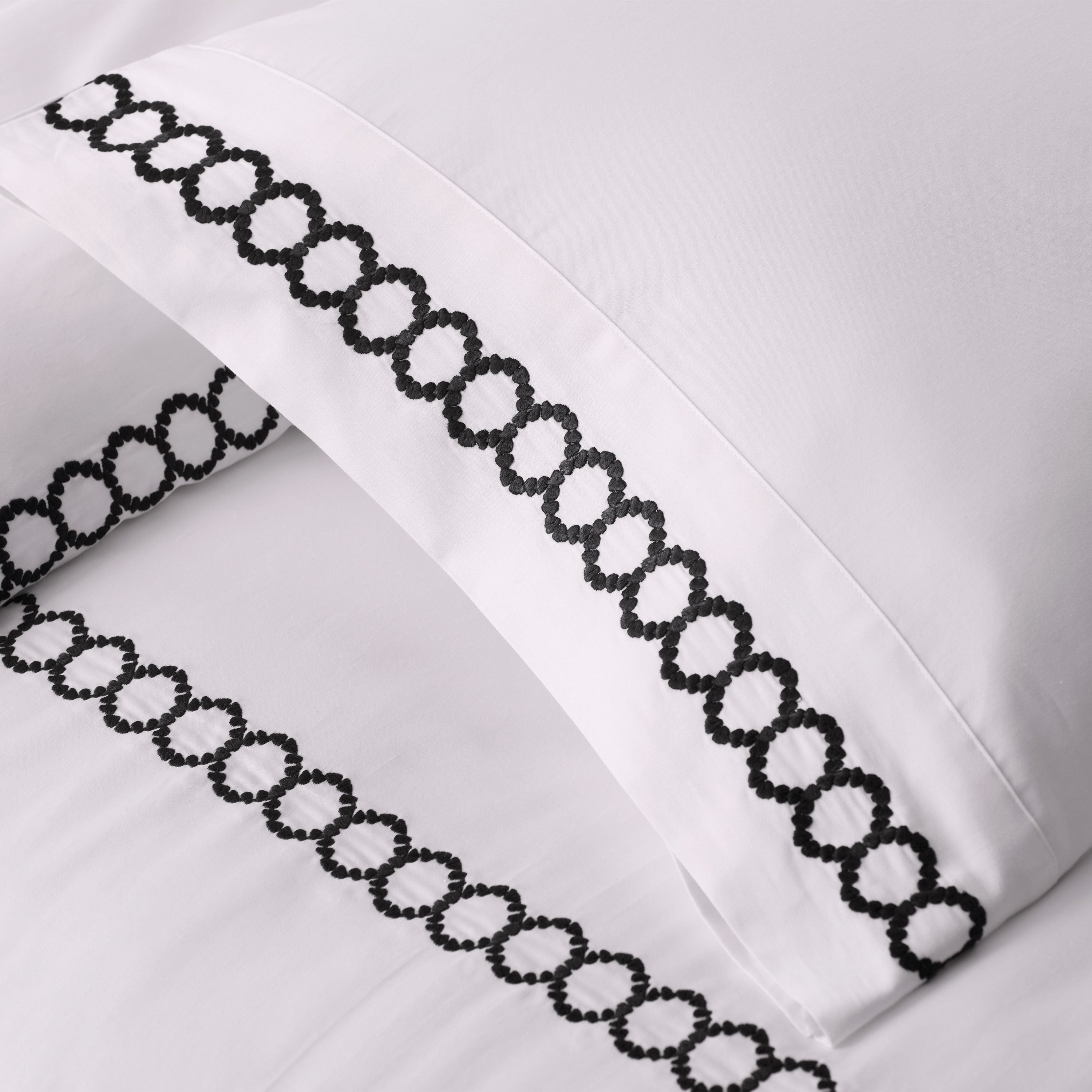 White bedding with black decorative stitching along the edges of the pillowcases.