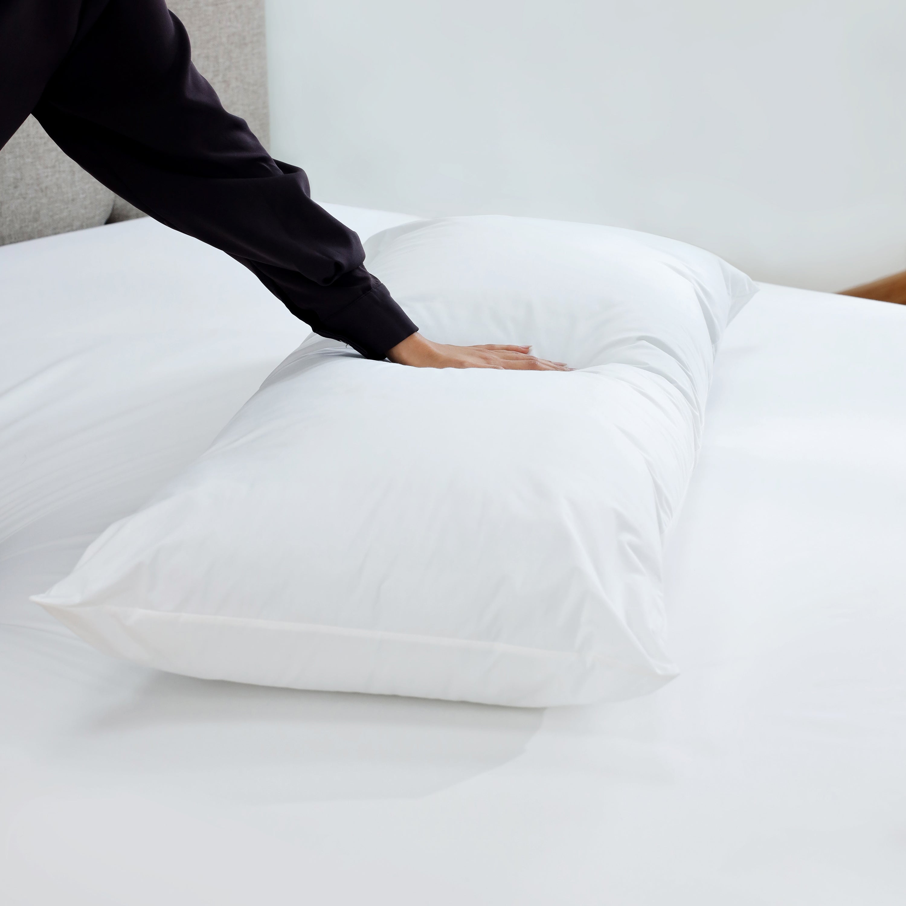 White gusset pillow on a bed with a hand resting on it, showcasing its soft surface and clean design.
