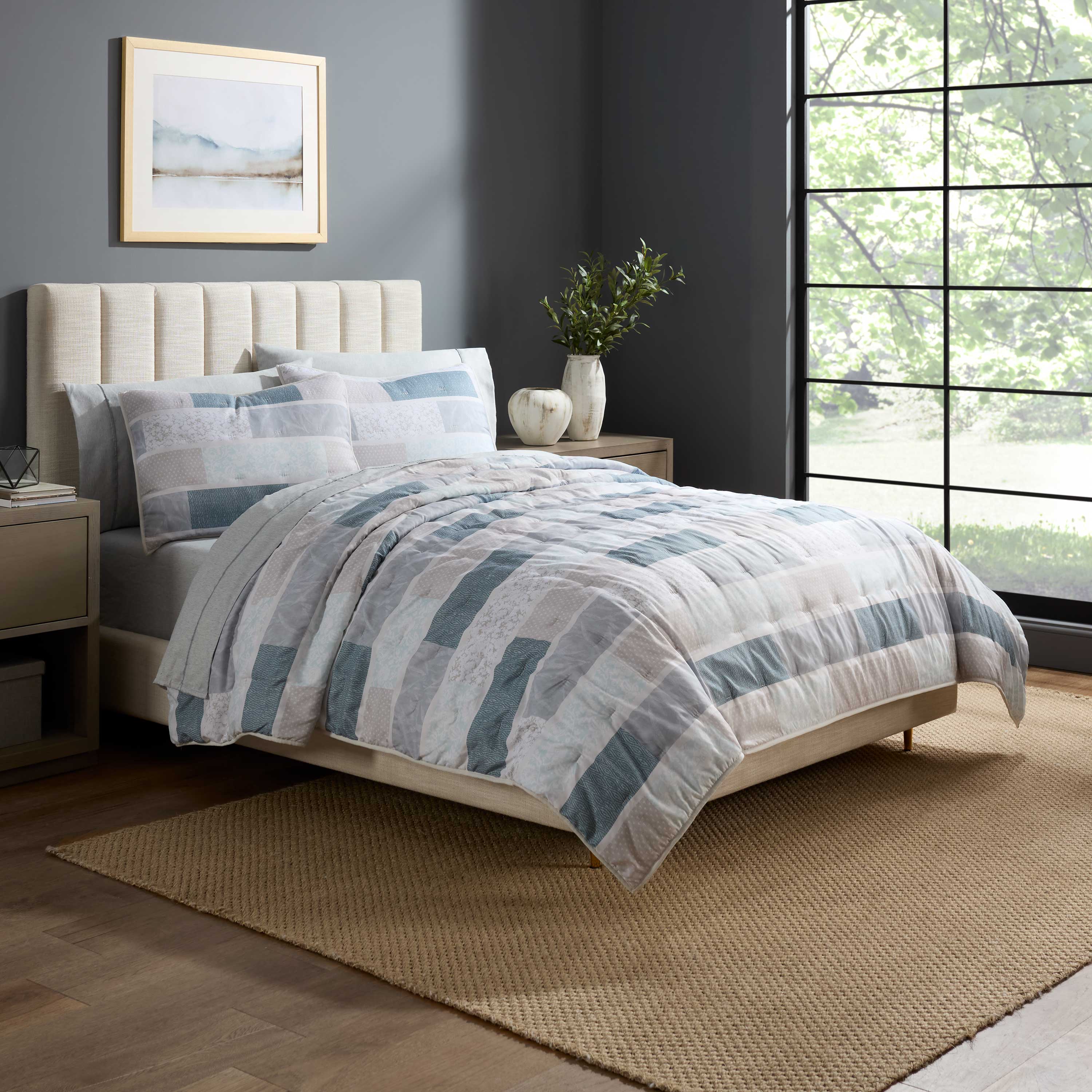 Quilt set featuring a patchwork design in shades of blue and gray, displayed on a bed with matching pillows.