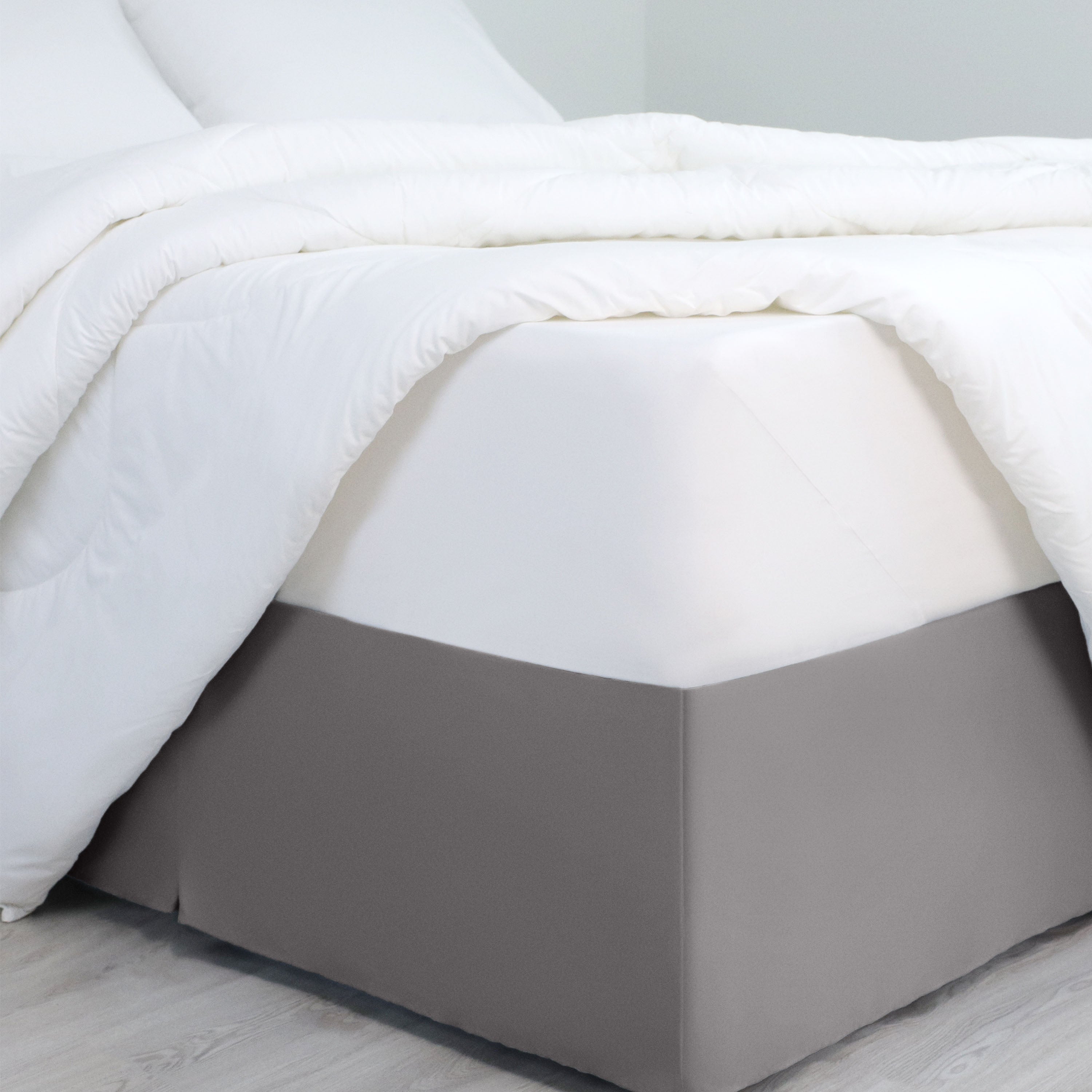 Bed skirt with inverted pleats in a solid gray color, draping over the base of a bed with white bedding.