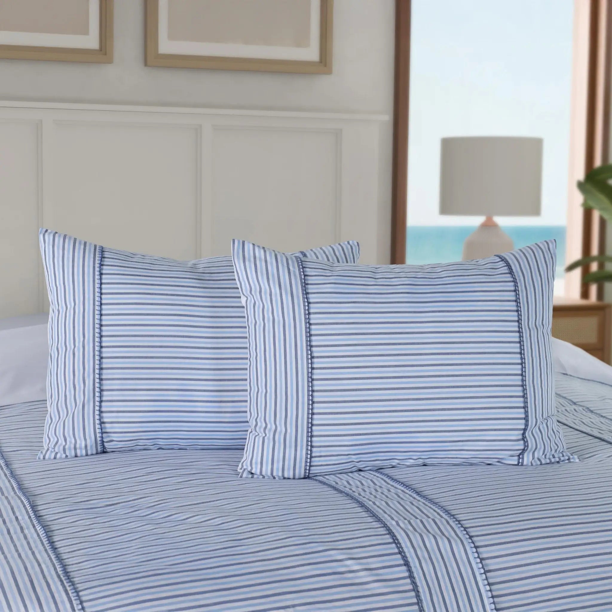 Blue striped comforter set with matching pillow shams on a bed in a bright bedroom.