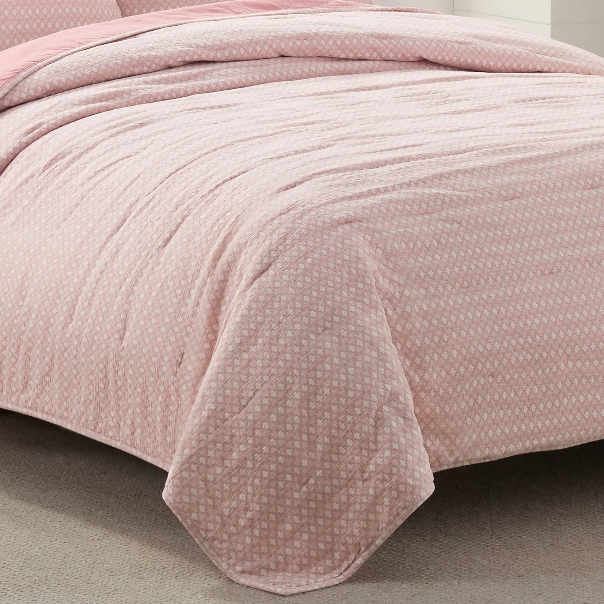 Pink textured quilt on a bed with a neutral background