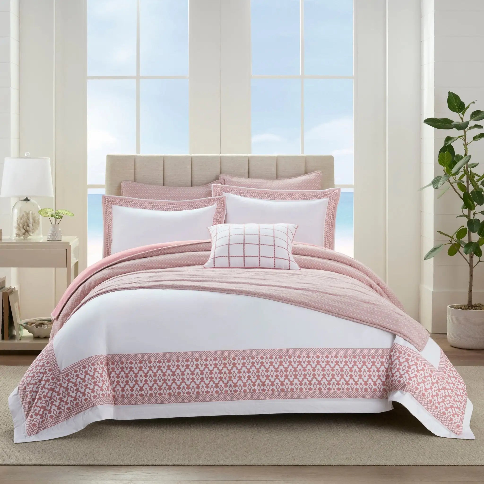 Bed with pink and white comforter set in a bright room with large windows.