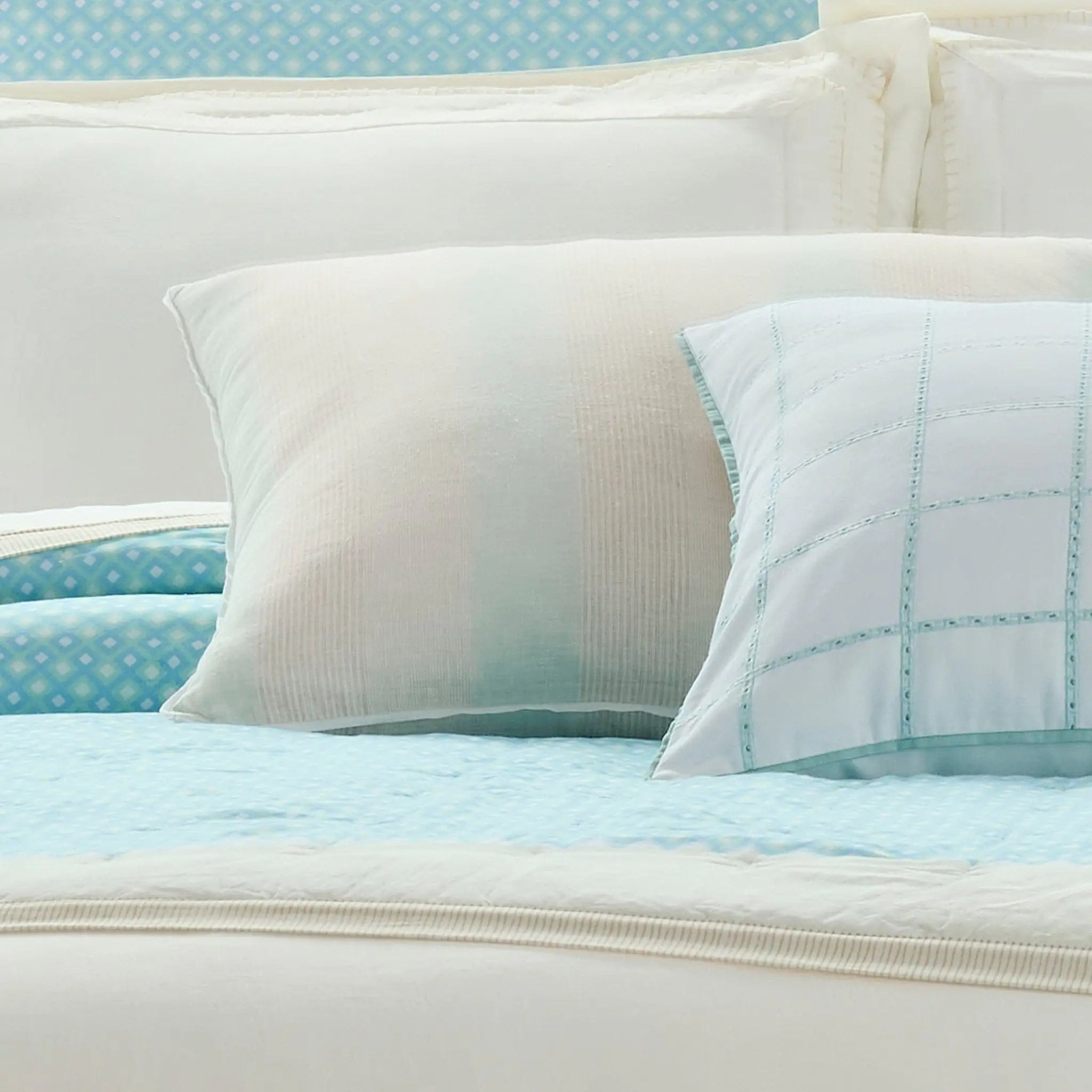 A close-up of a bed styled with white pillows and a light blue patterned quilt and matching pillow shams.