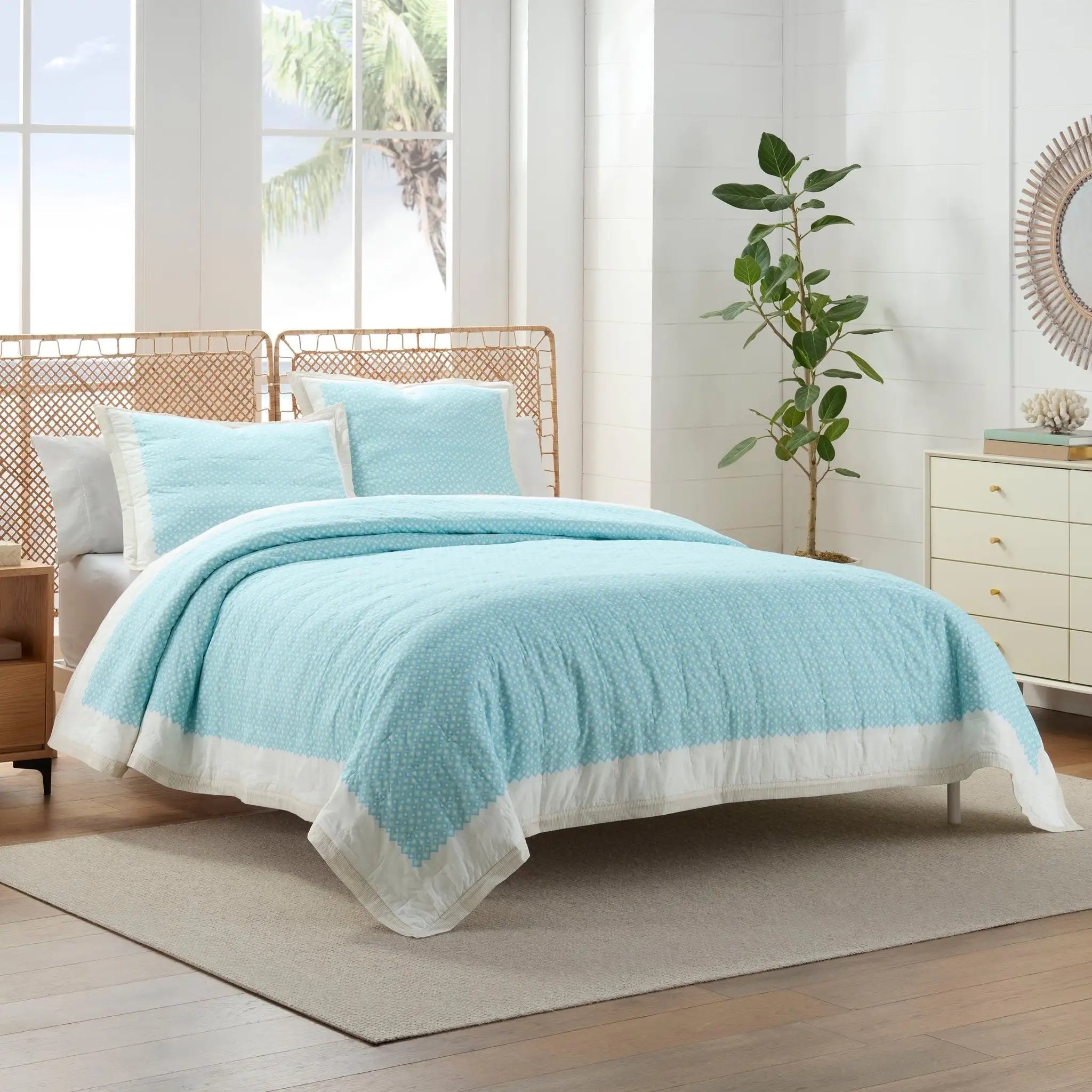 A light blue and white textured quilt set on a bed in a bright, modern bedroom.