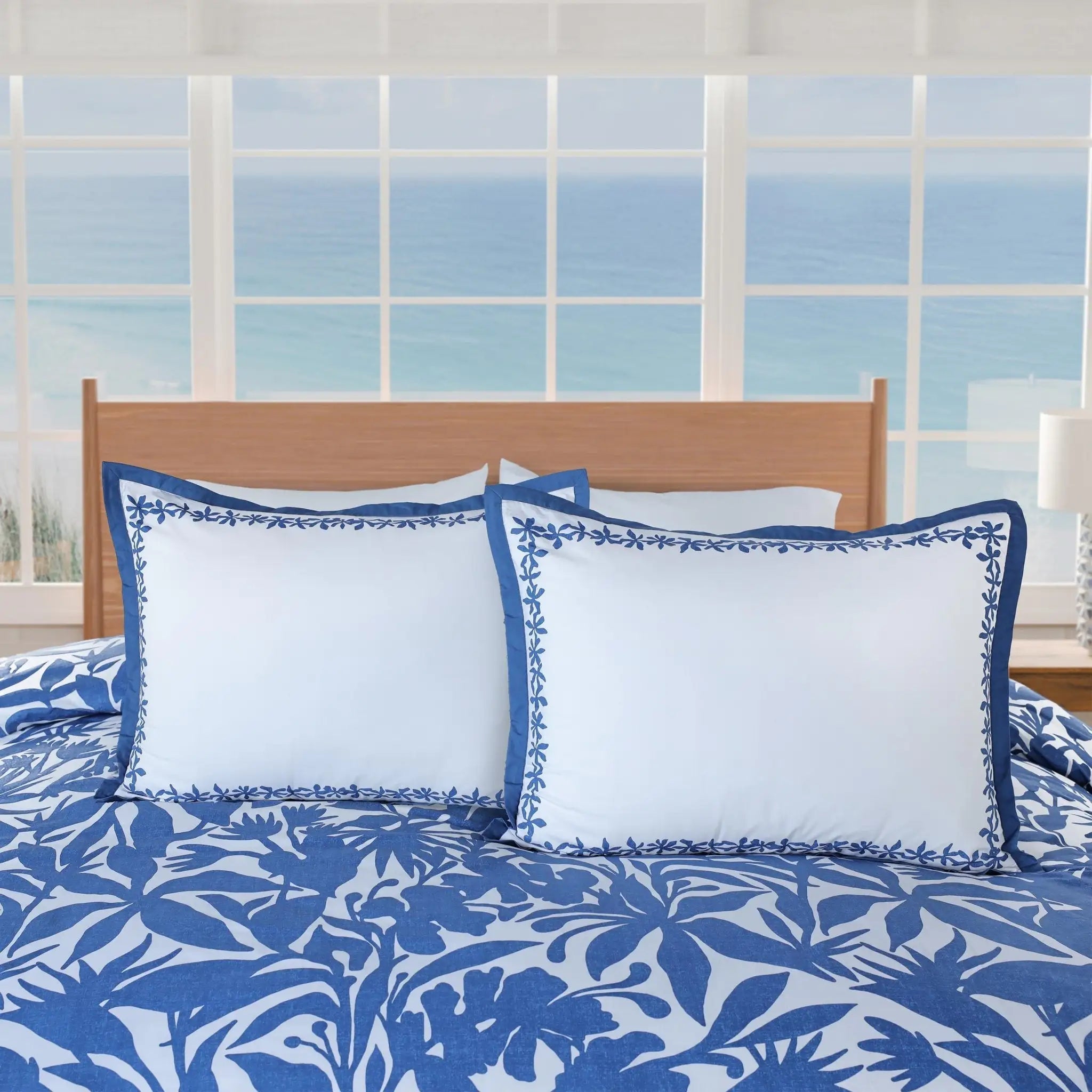 A bed styled with a blue and white tropical floral print comforter, two matching blue-trimmed white pillow shams.
