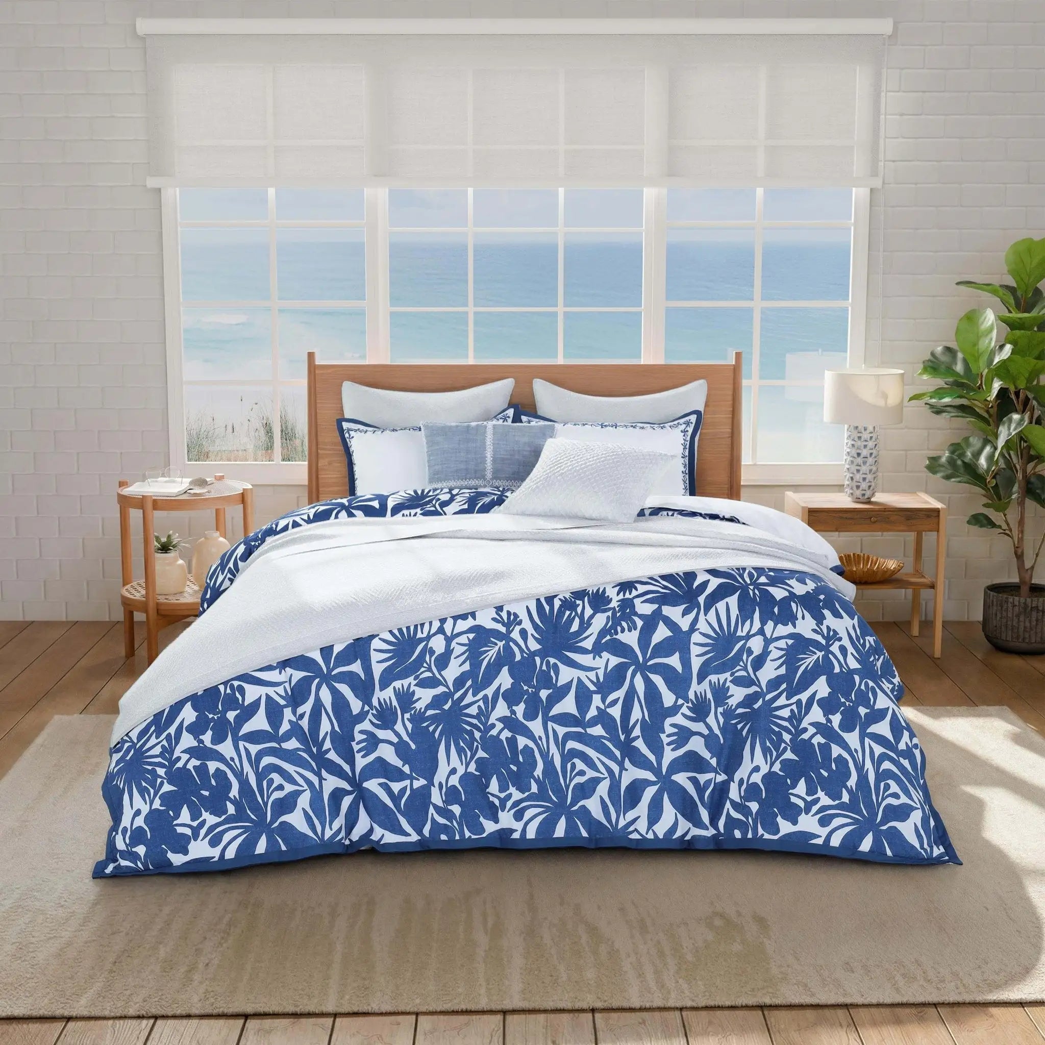 A bed dressed in a blue and white tropical palm leaf patterned comforter set.