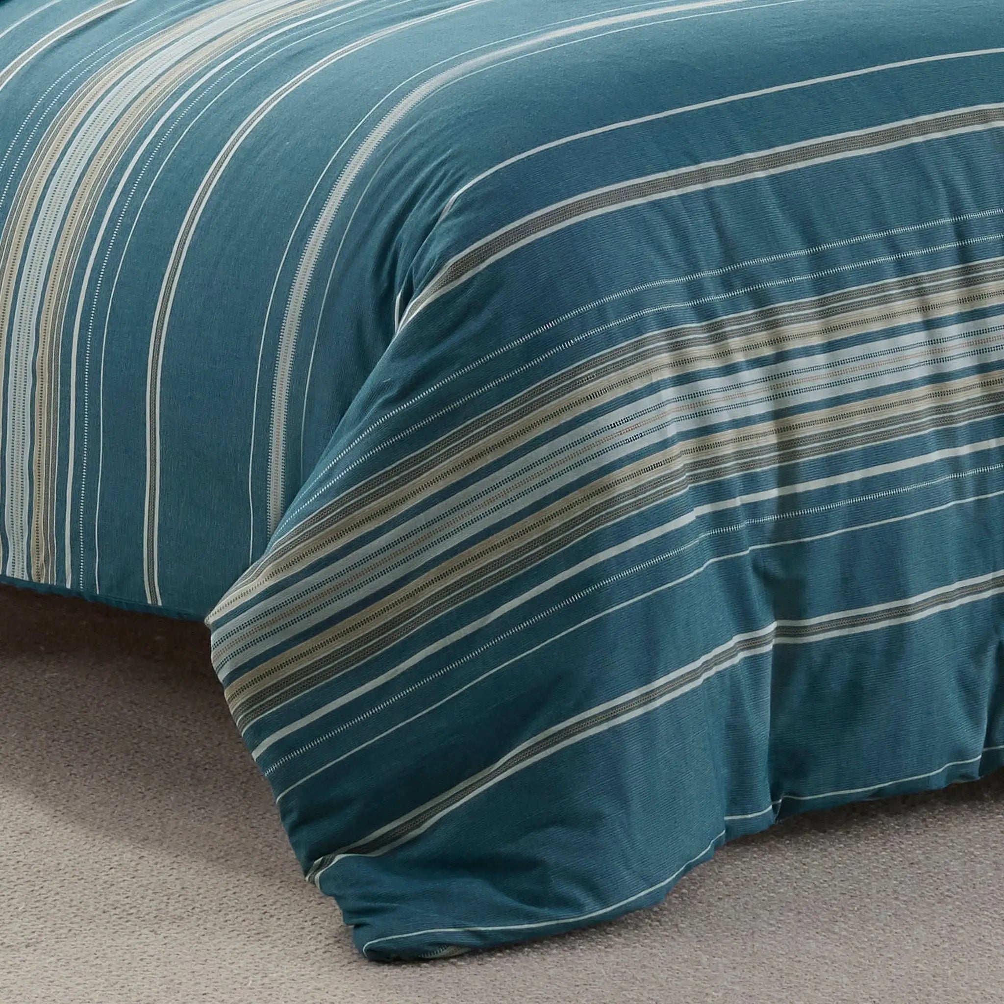 Close-up of blue striped comforter on a bed with a beige carpet.