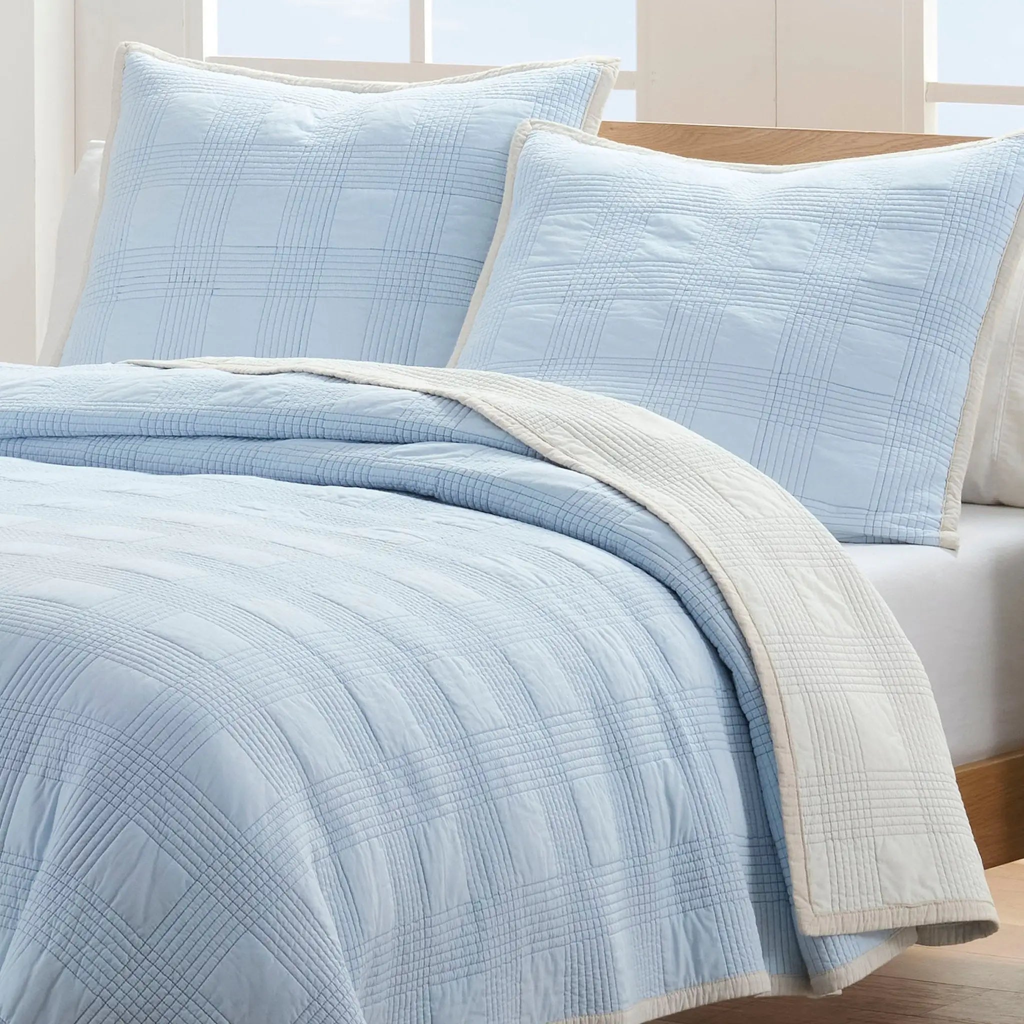 Light blue textured quilt set on a bed with euros.