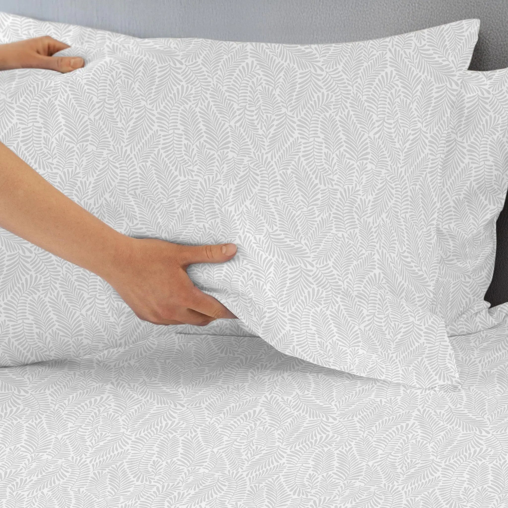 Person adjusting a white pillowcase with a subtle pattern on a bed.