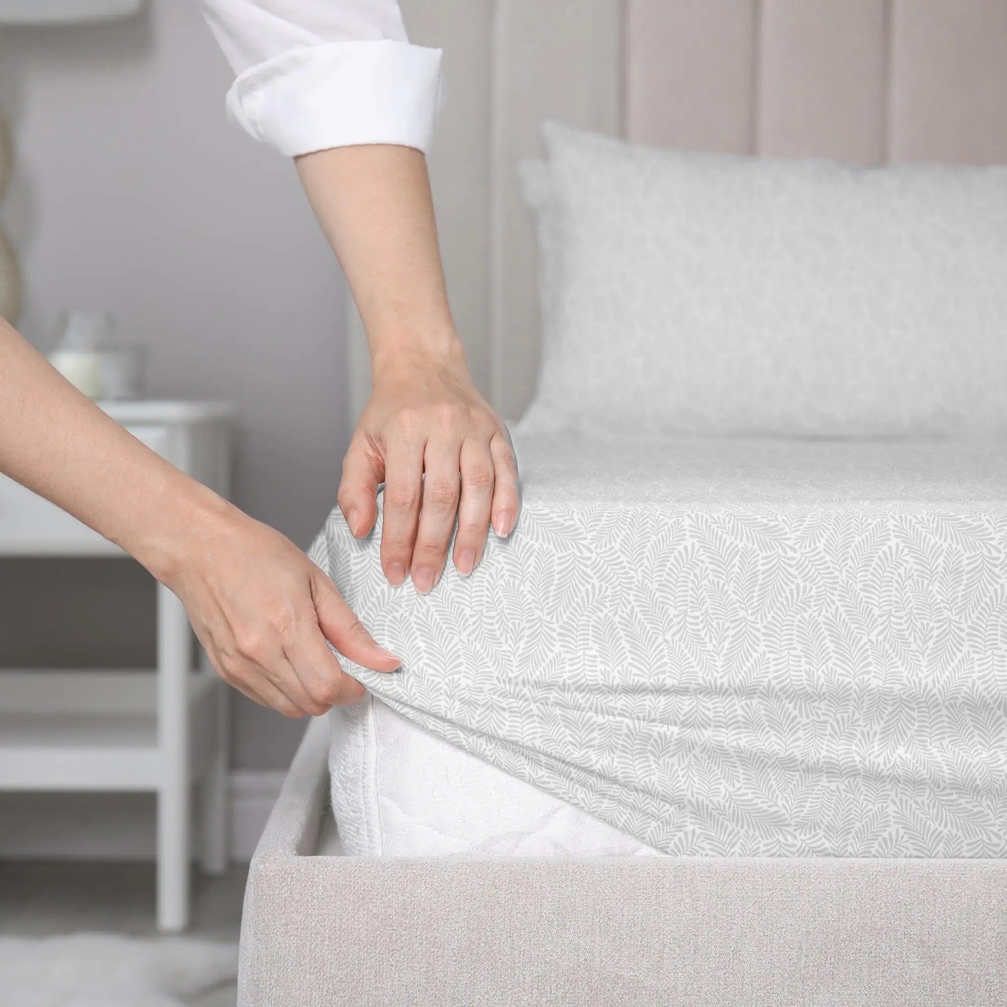 Person adjusting a fitted sheet on a bed in a bedroom setting
