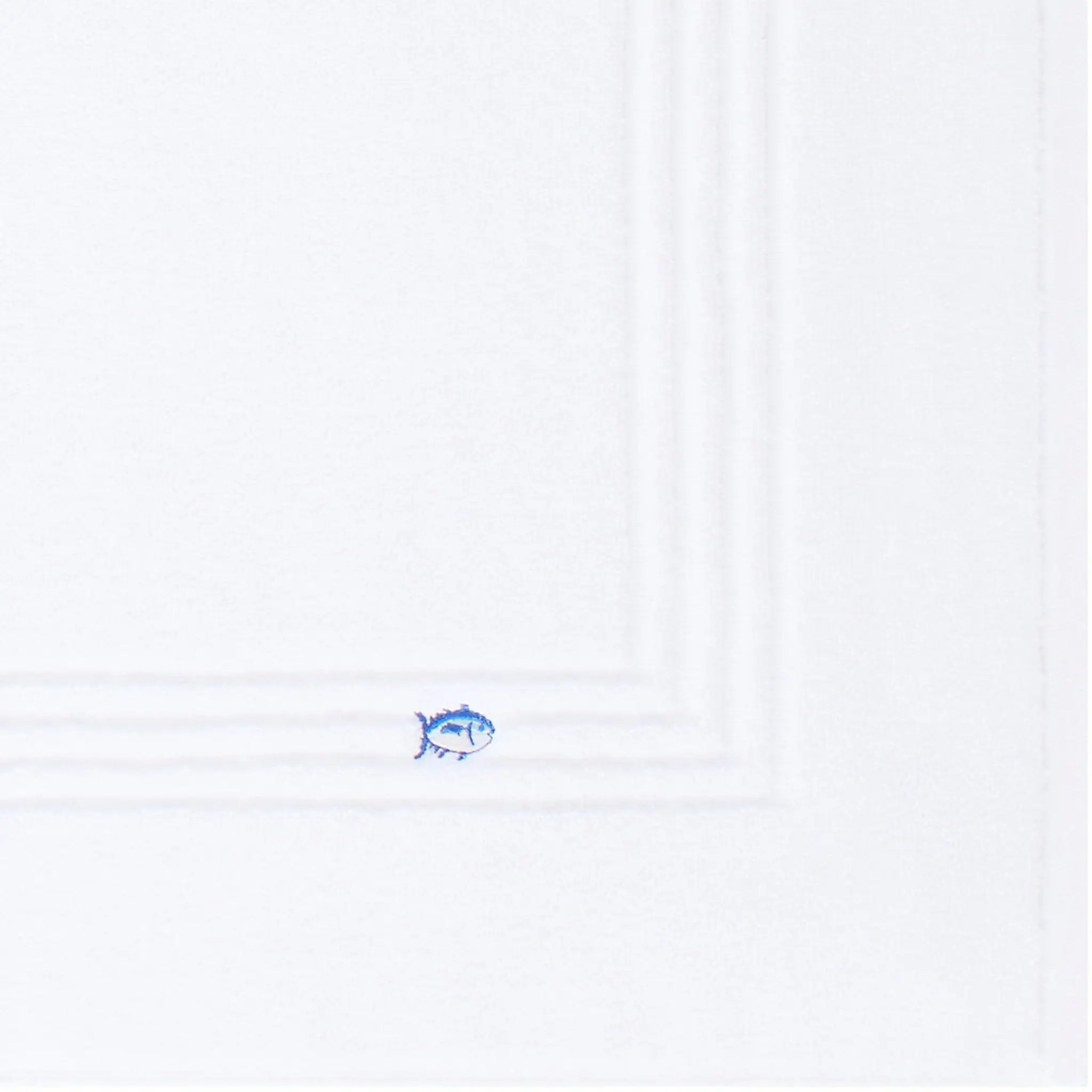 A close-up of a white bath mat surface, with a small blue fish emblem near the bottom edge.