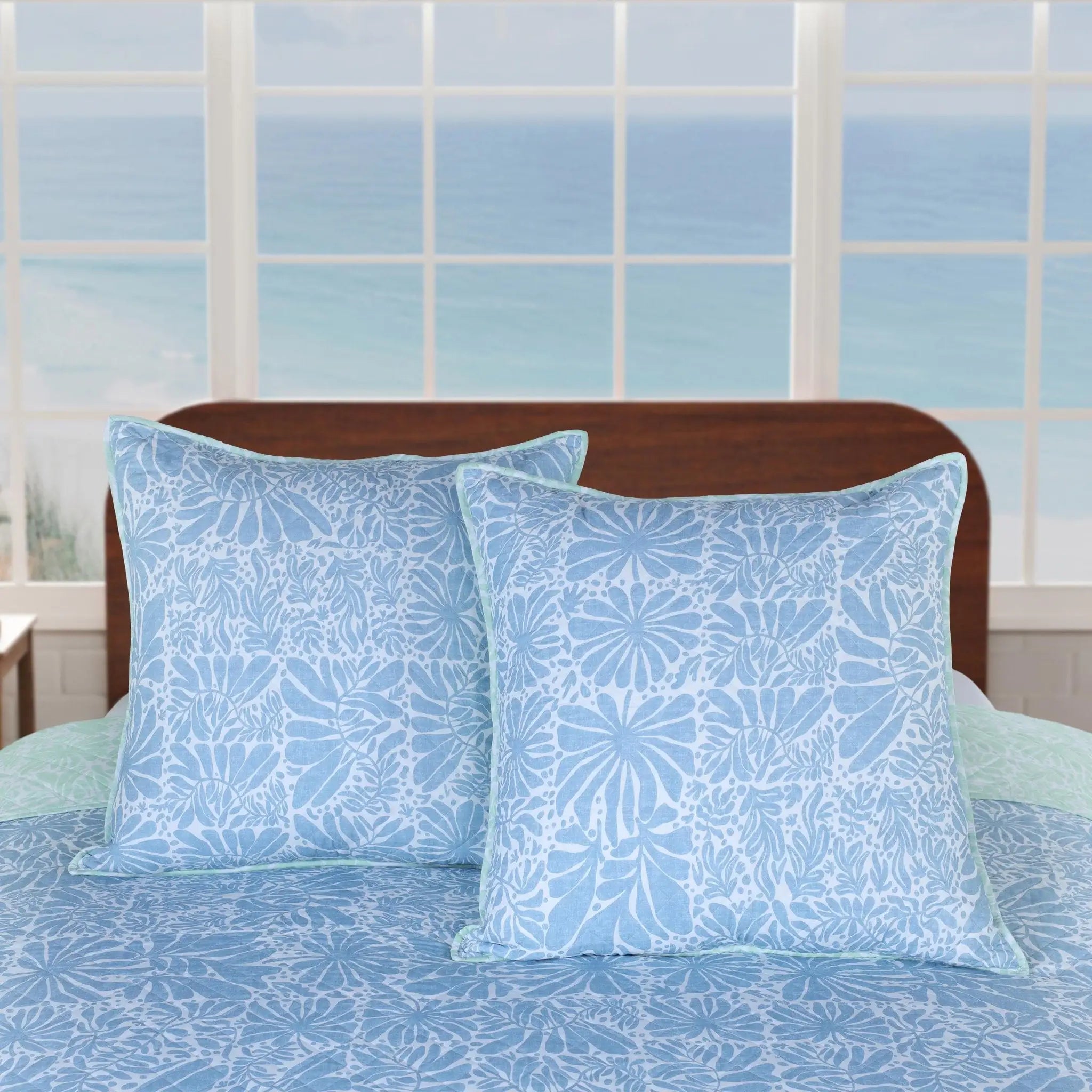 Blue patterned euros on a bed with a window in the background