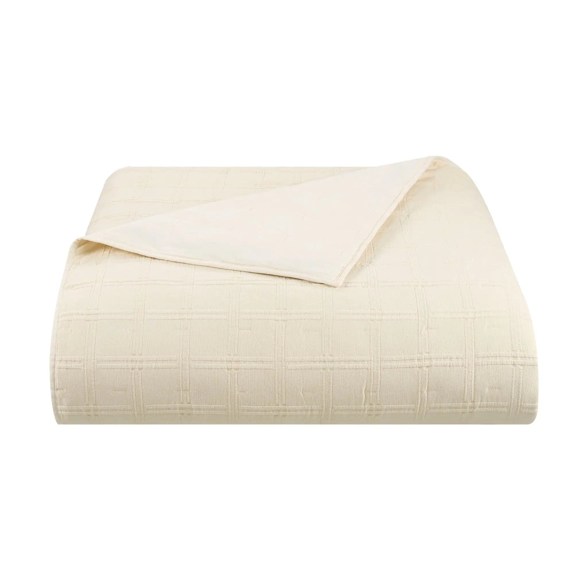An ivory quilt with a subtle grid pattern, folded neatly with one corner folded over, shown on a solid white background.