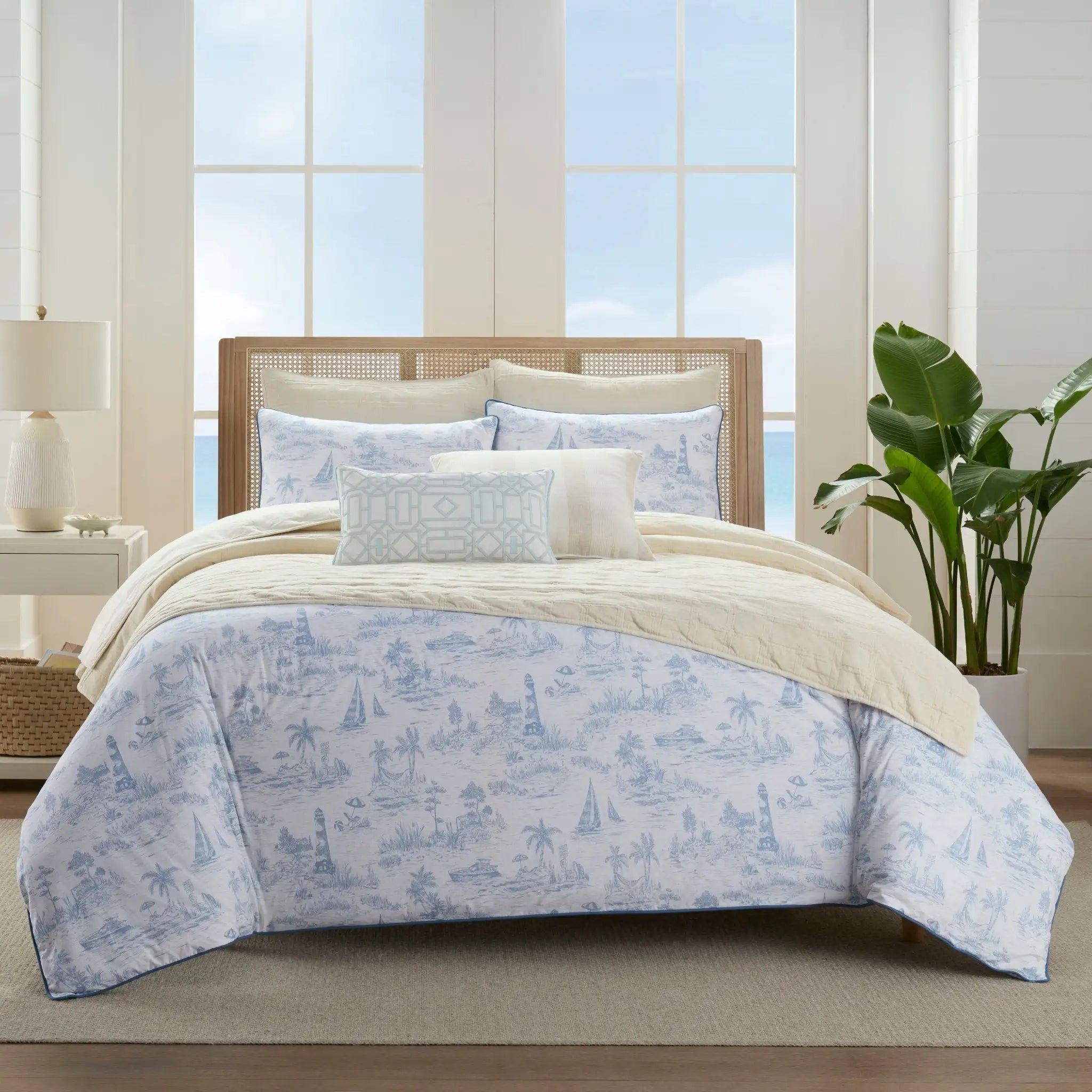 A beautifully made bed in a bright, modern bedroom featuring a light blue and white toile-patterned comforter set.