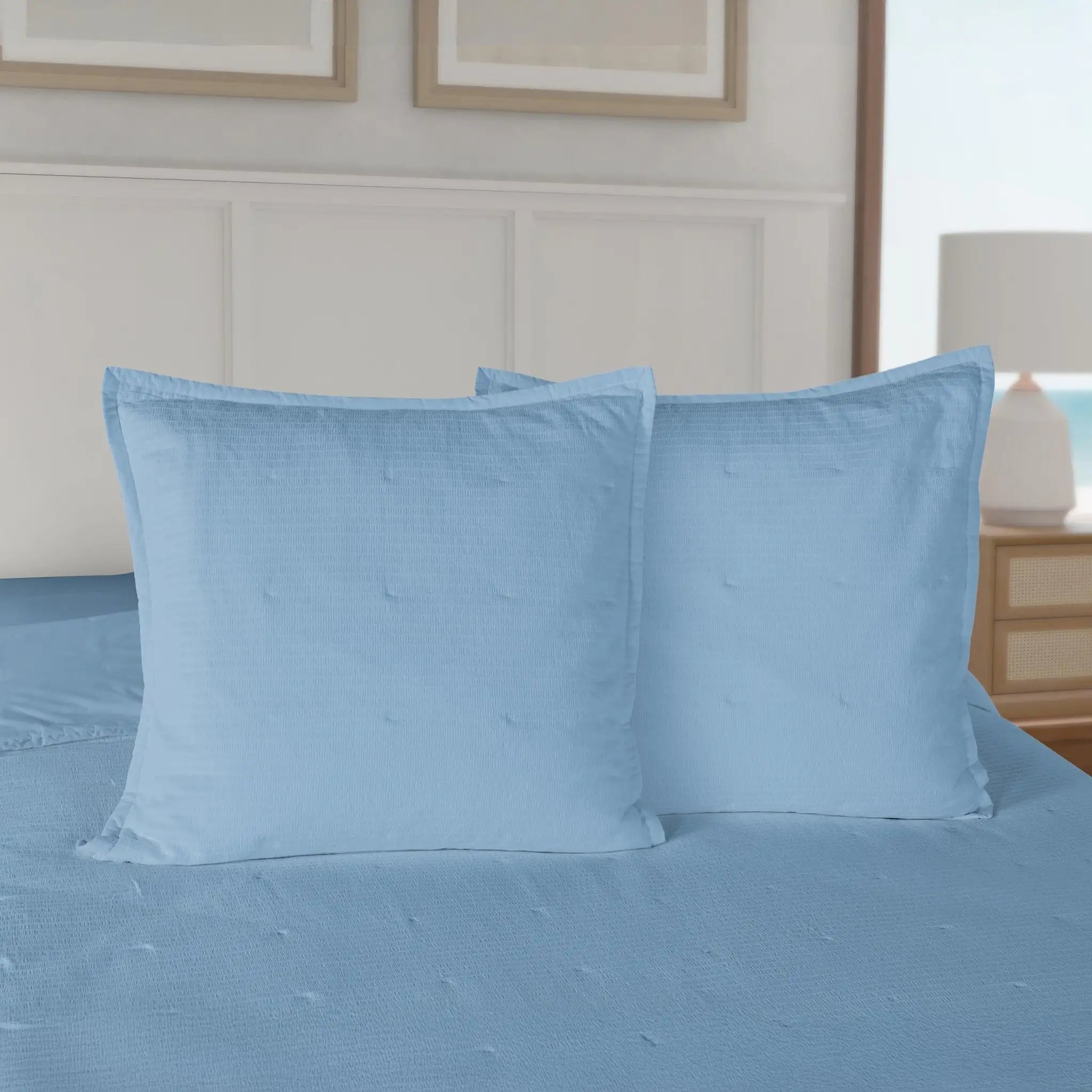 Blue quilt and euros on a bed in a bedroom setting.