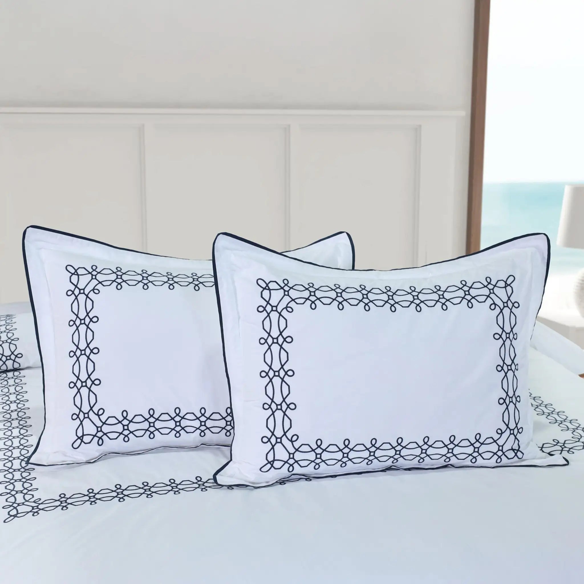 Two white pillow shams with navy embroidery on a bed.
