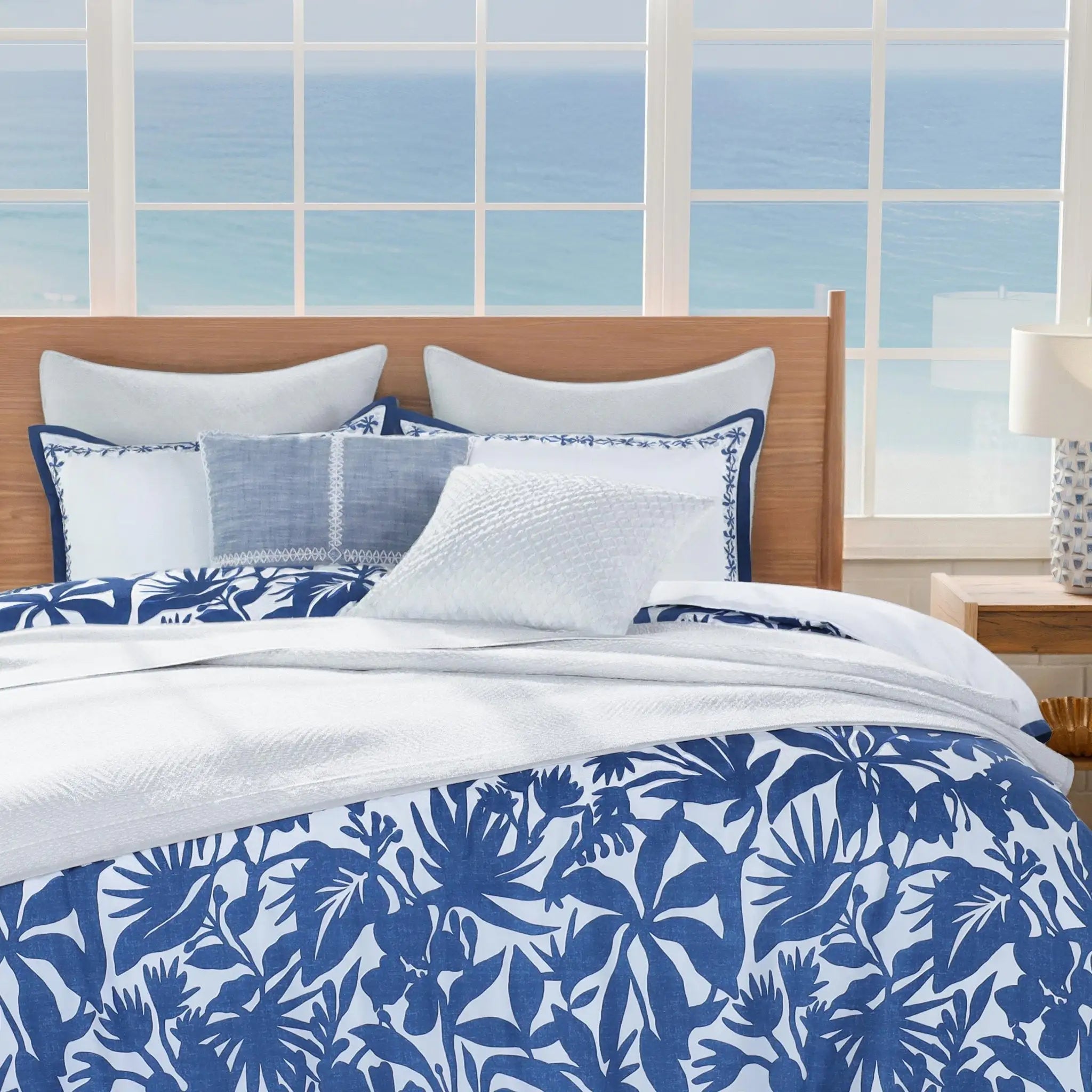 Bed with blue and white floral bedding in a room with large windows showing an ocean view.