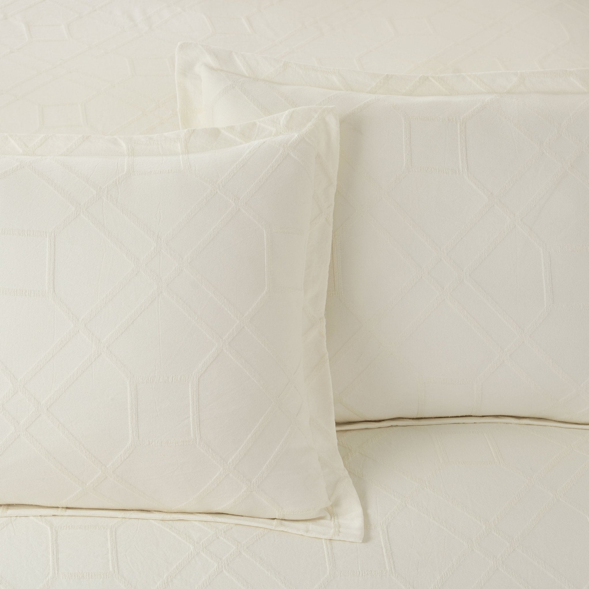 Close-up of ivory quilted comforter with pillow shams on a neutral background