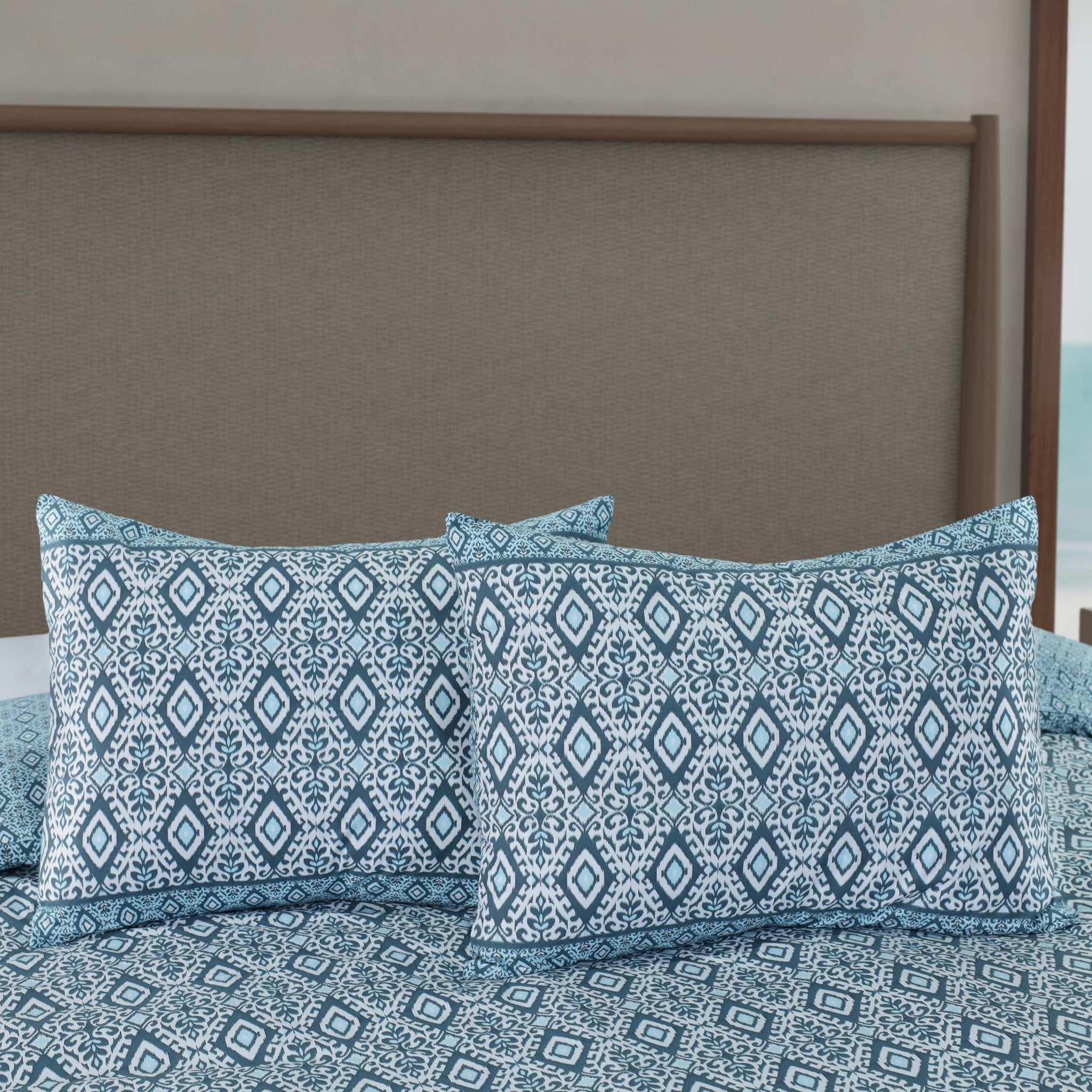 Blue and white patterned shams on a bed with a brown headboard.