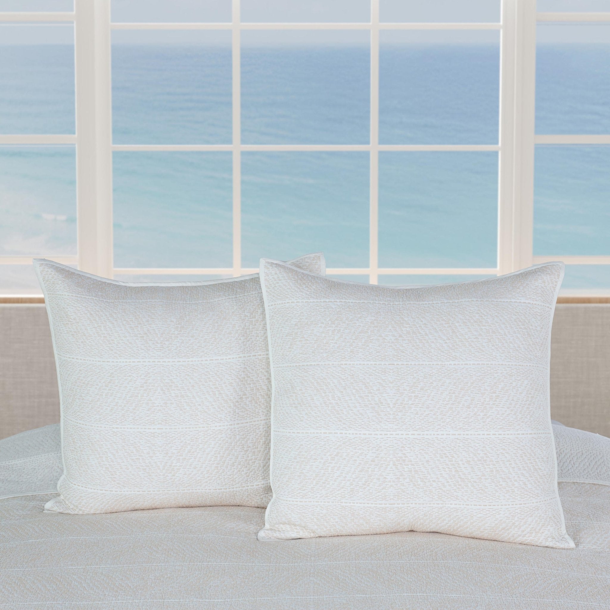 Two white pillows on a bed with a window in the background