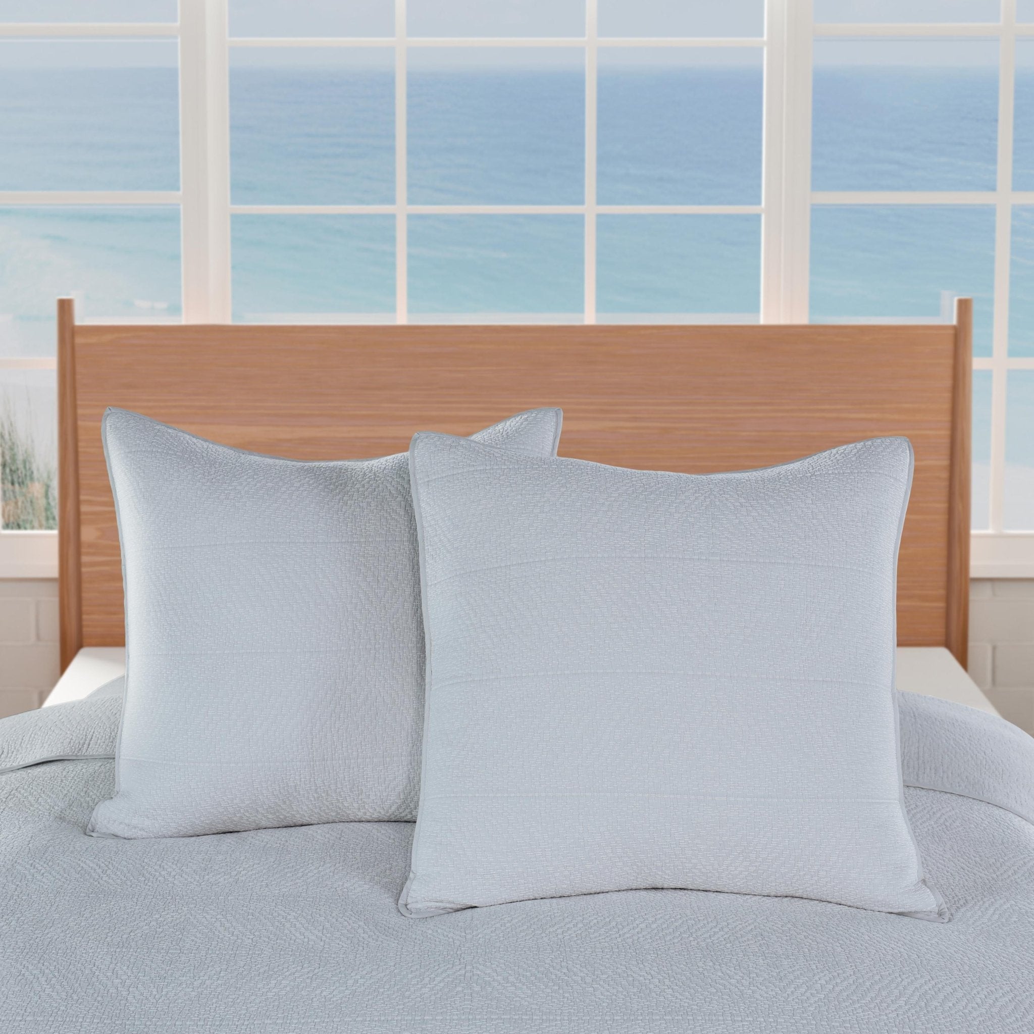 Two light blue pillows on a bed with a wooden headboard.