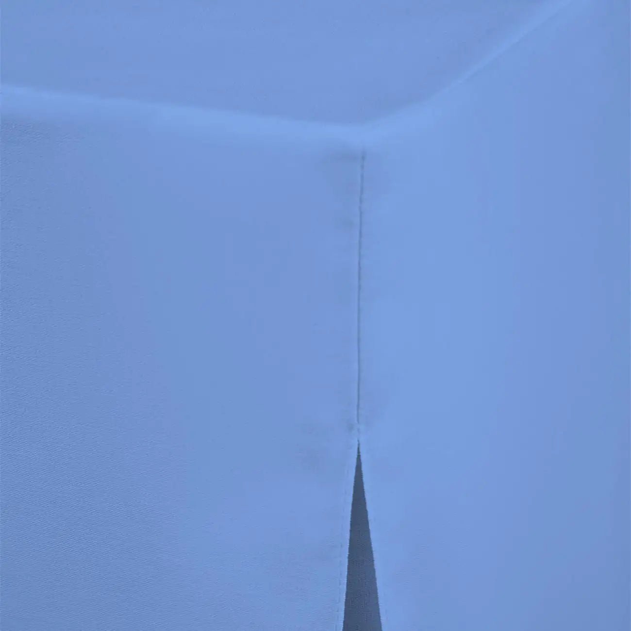 A close-up of a light blue fabric corner with a vertical stitched seam and a small slit opening at the bottom.